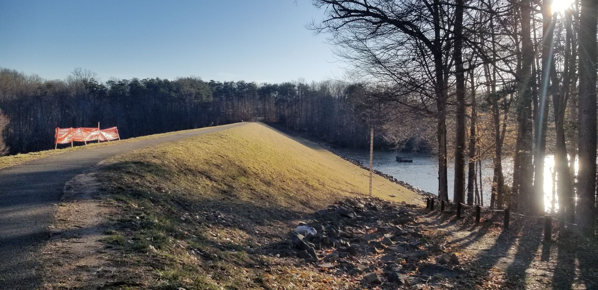 Sunny path on a grassy embankment next to a lake, with bare trees. - Lake Mercer – Barrel Vault Bridge - Lorton loop from Newington Forest