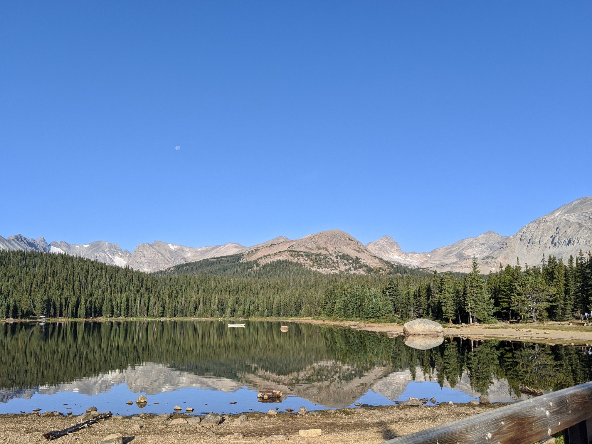 A clear mountain lake reflecting forested shores and rugged peaks under blue sky. - CMC South Trail and Little Raven Trail