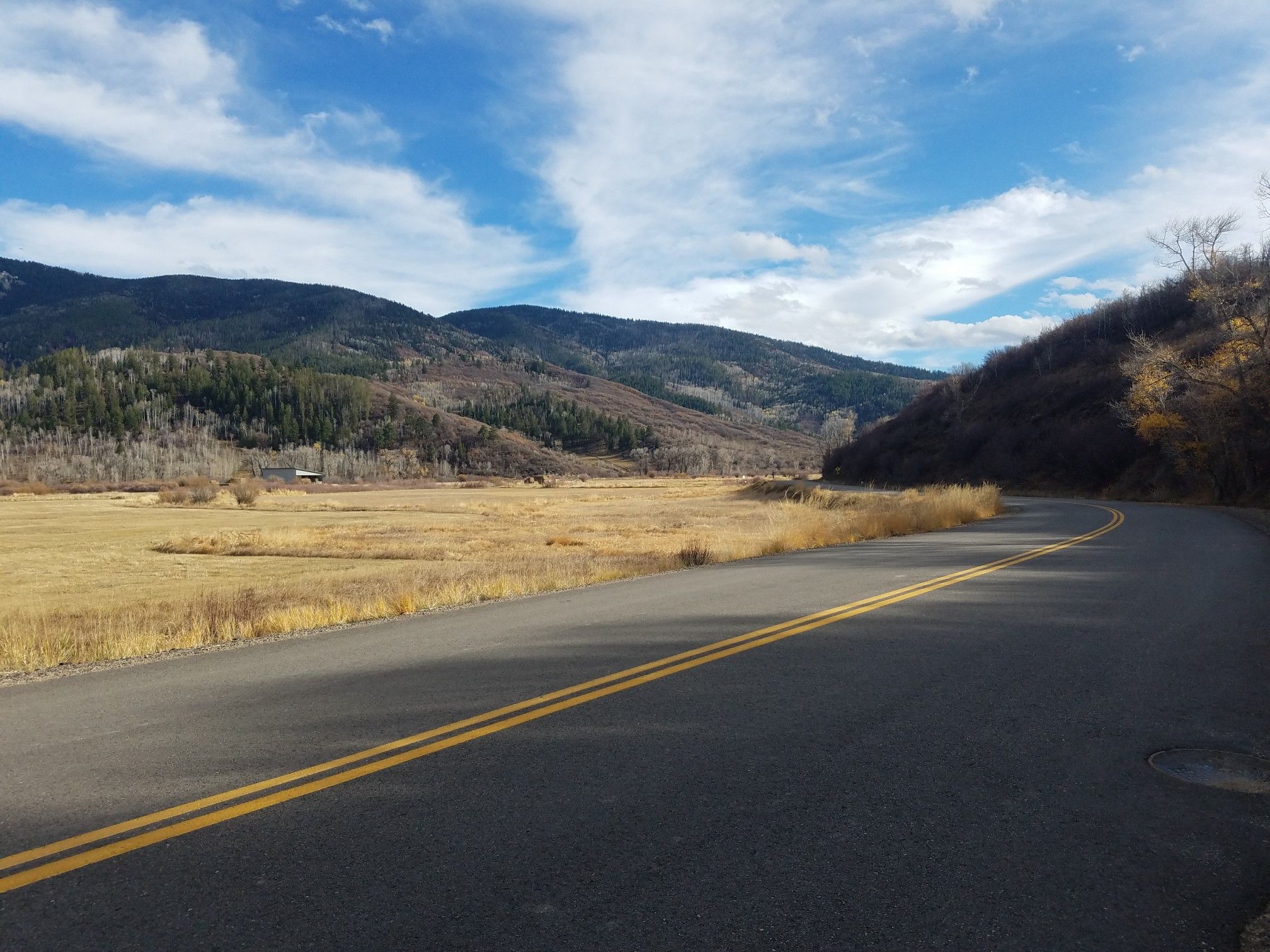 A paved road curves through golden fields with forested mountains under a cloudy sky. - Lake Catamount – Lake Catamount loop from Pleasant Valley Airport