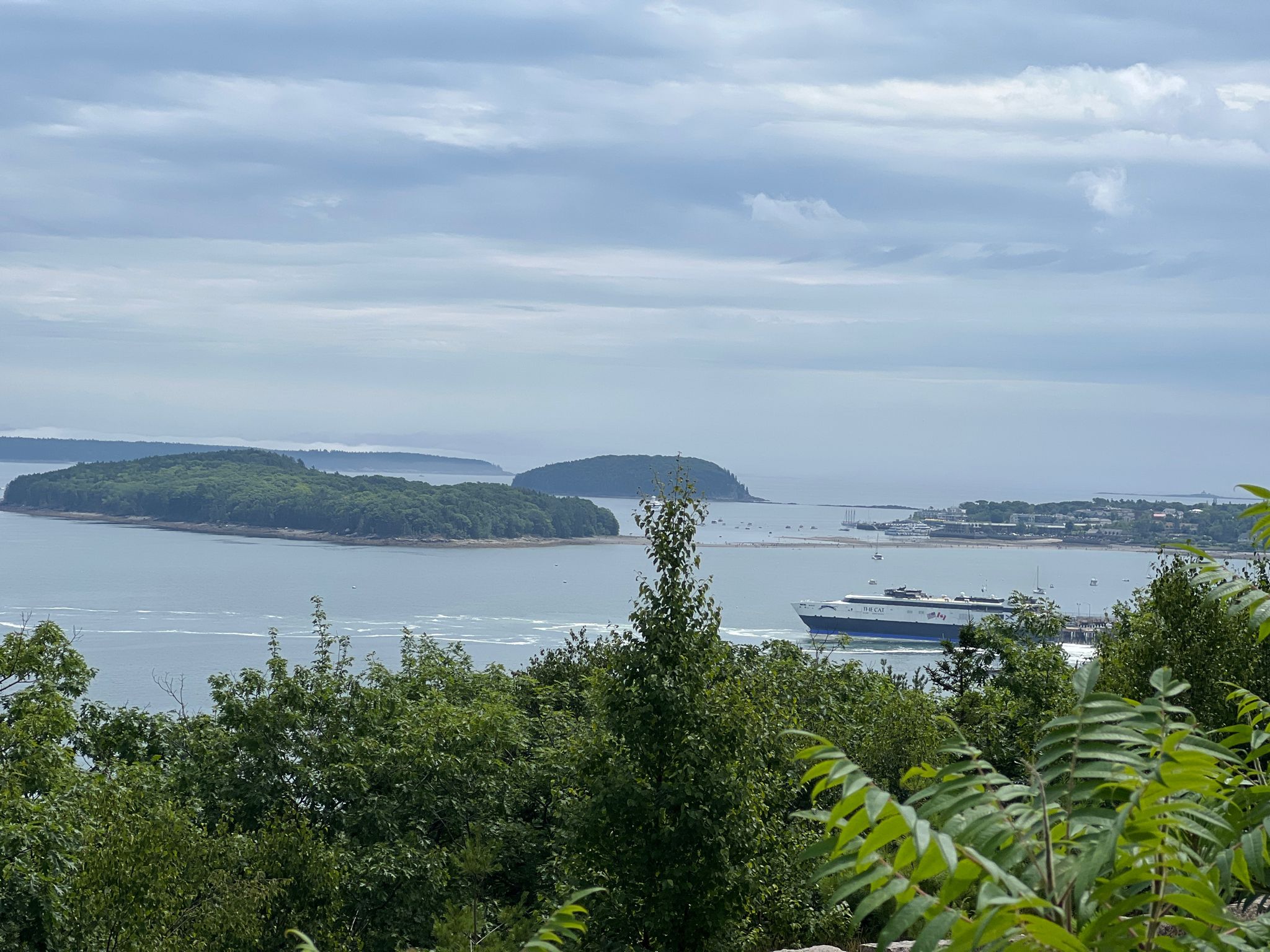 Overcast coastal view with green islands, a large boat, and distant land. - Bass Harbor Head Light and Acadia National Park loop