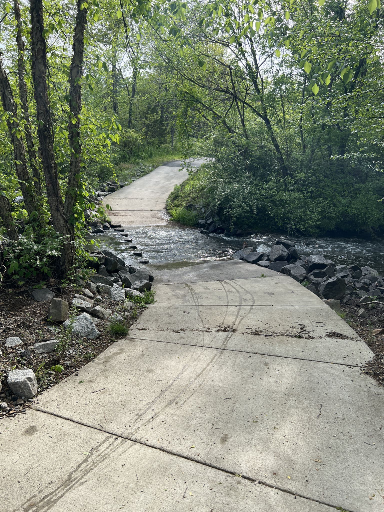 Concrete path descends into a flowing stream surrounded by green trees. - Green Lizard Cycling, Herndon – Herndon Caboose Park loop from Loudoun Gateway