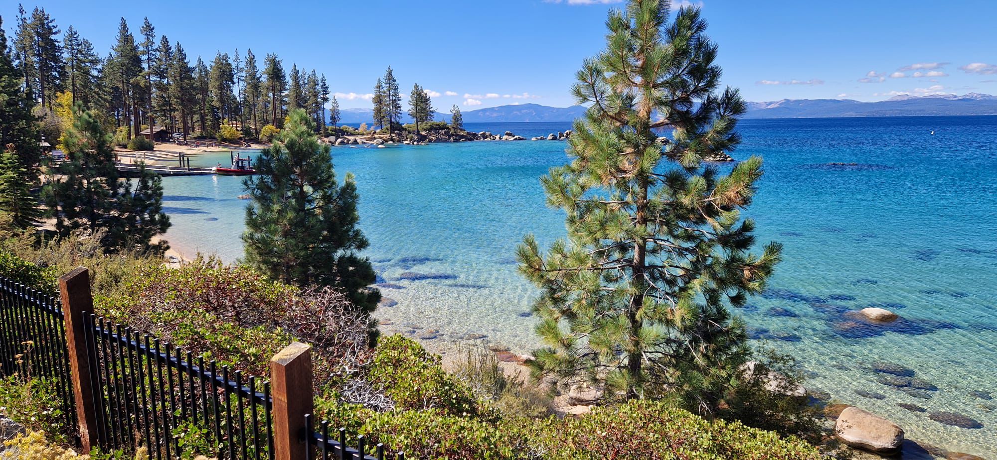 Clear turquoise water, sandy beach, pine trees, distant mountains, sunny. - Lakeshore Blvd Bike Path