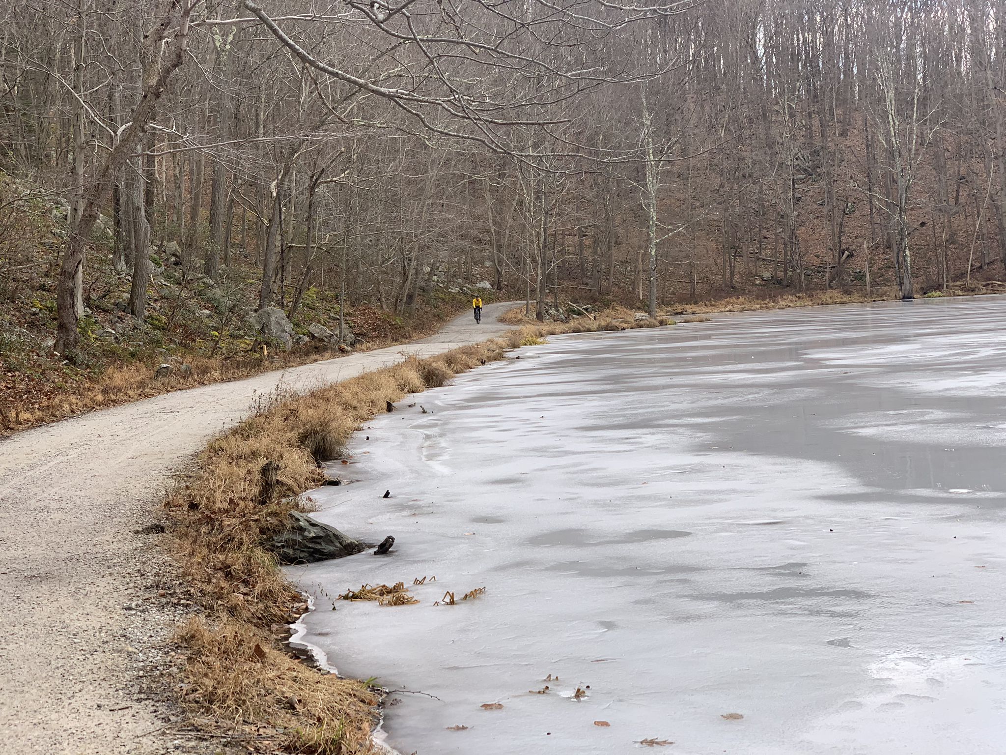 A person walks on a dirt path beside a partially frozen lake in winter. - Sunken Mine Road – Indian Brook Road - gravel loop from Cold Spring