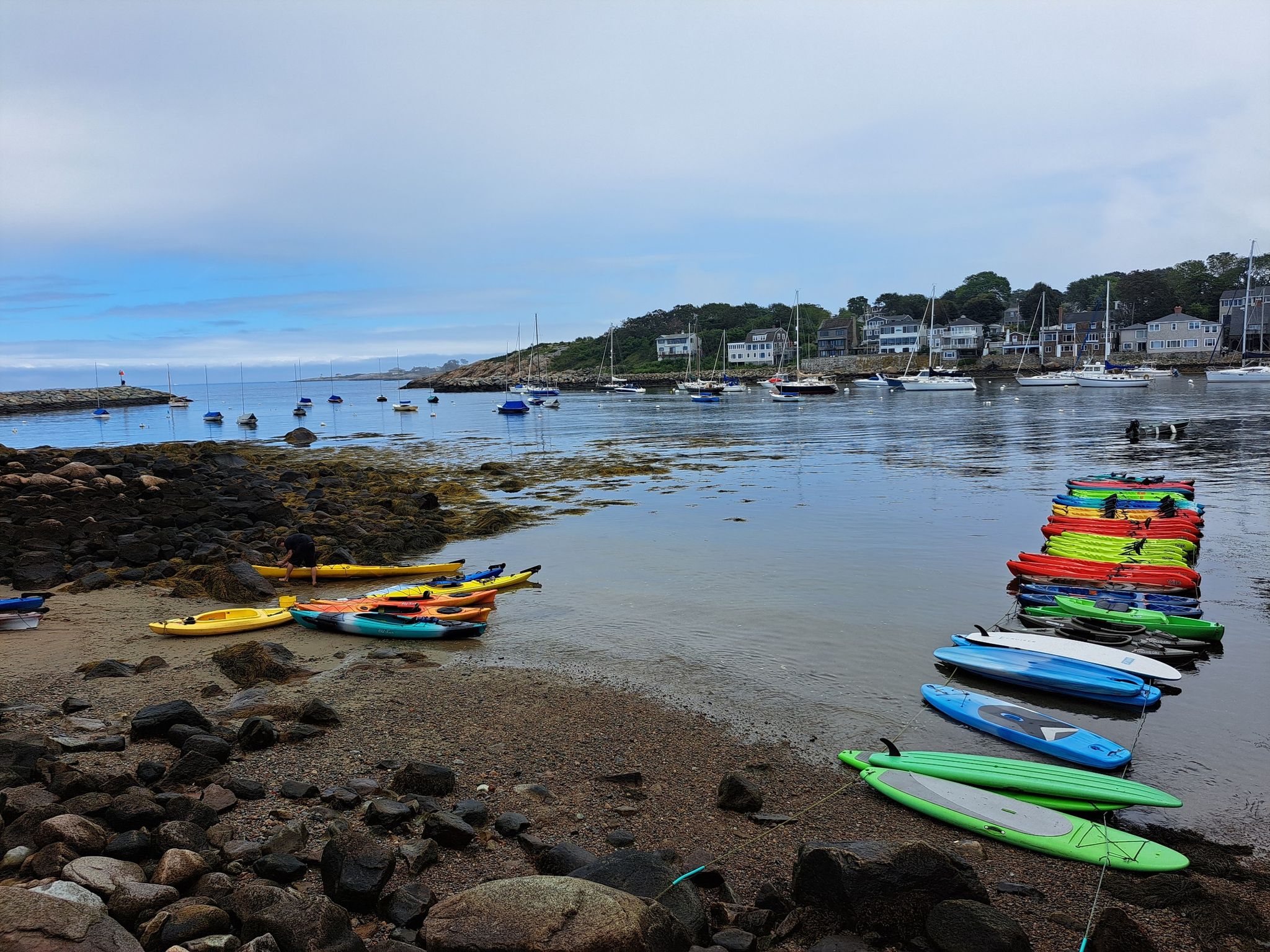 Colorful kayaks and paddleboards line a sandy beach next to a calm bay. - Bearskin Neck and The Headlands Loop