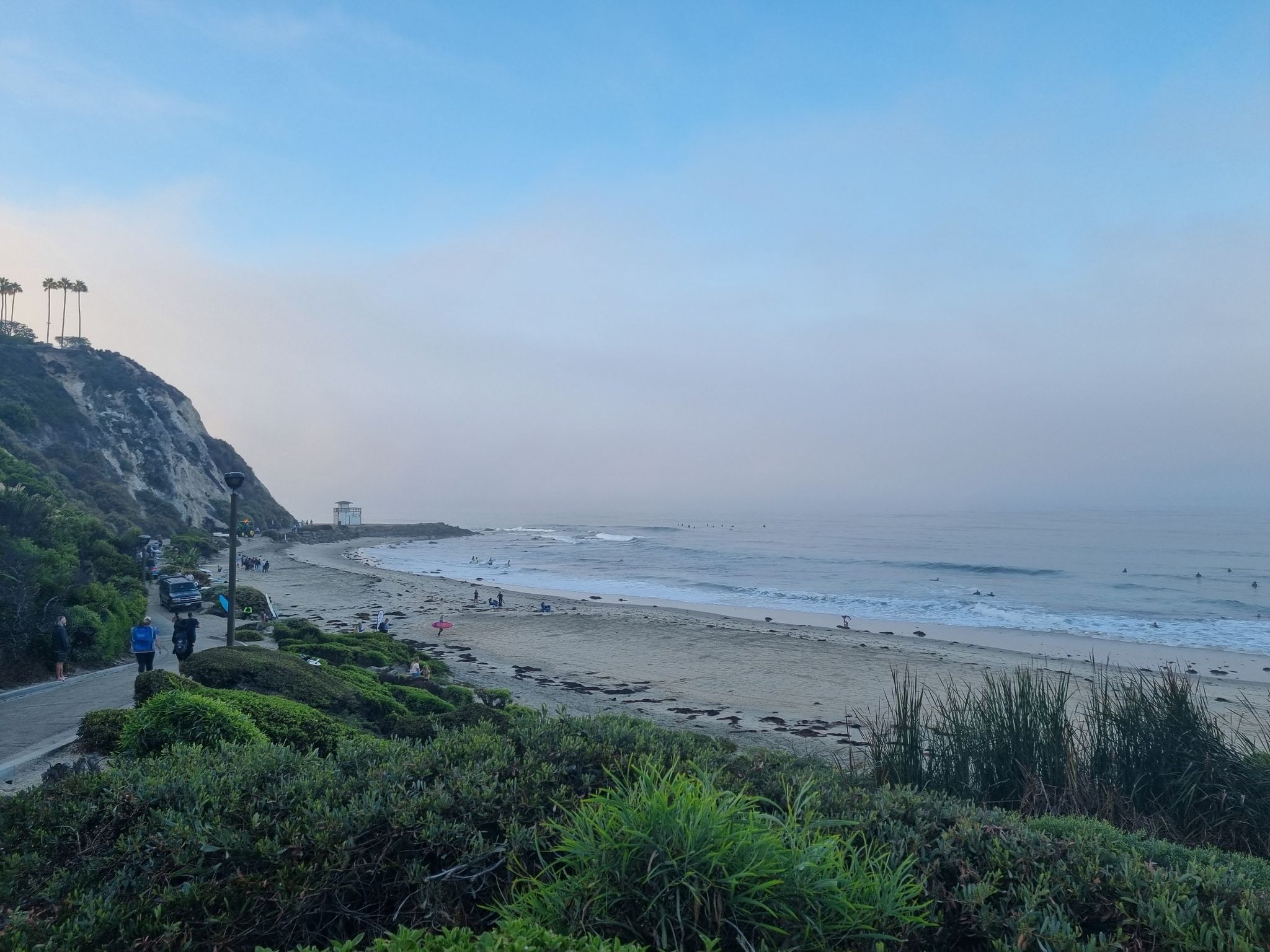Hazy coastal scene with beach, ocean waves, and people on a paved path. - Salt Creek Beach loop from Dana Hills High School
