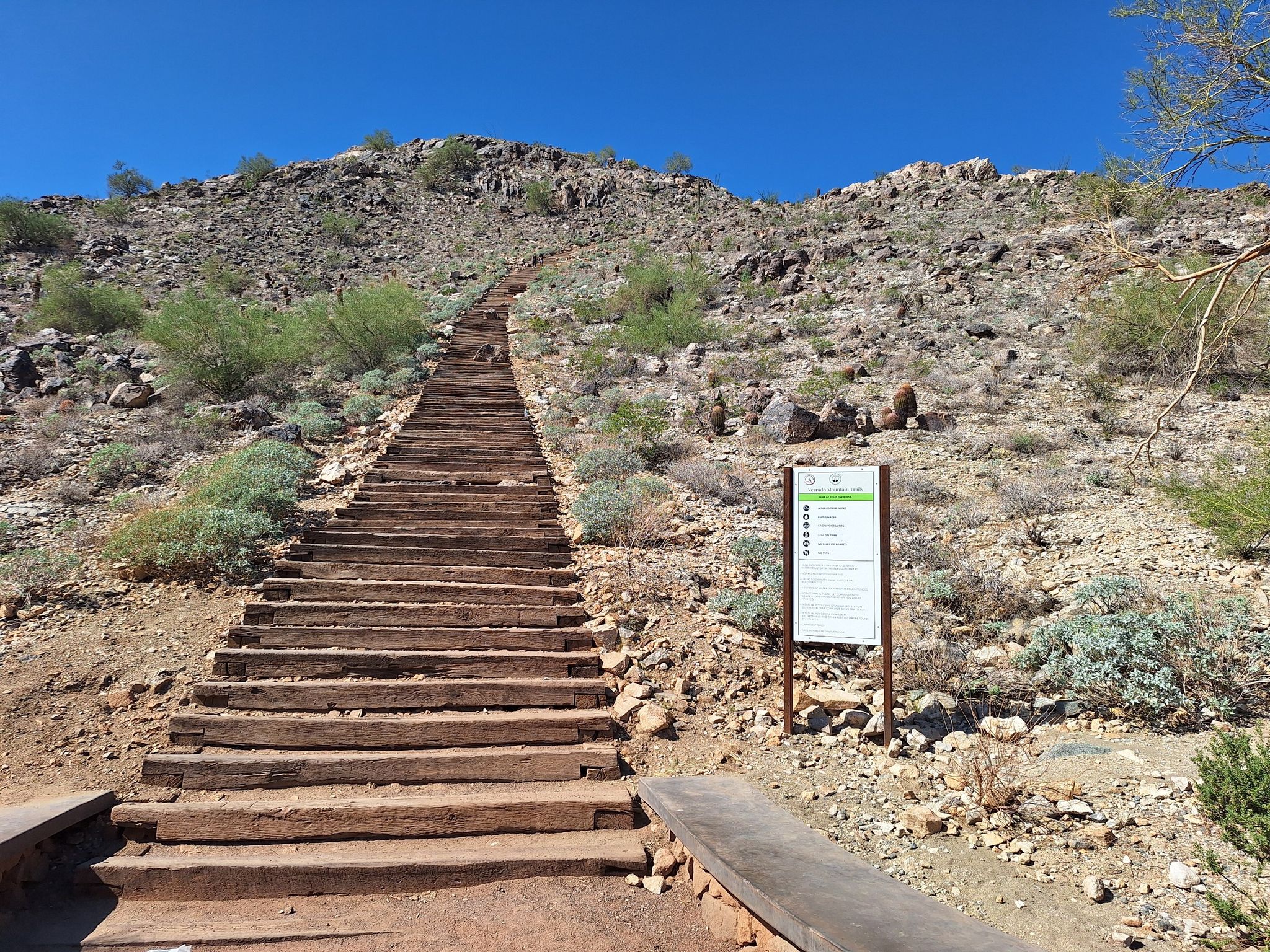Long wooden staircase ascending a rocky desert hill with a trail sign. - Verrado Mountain Loop