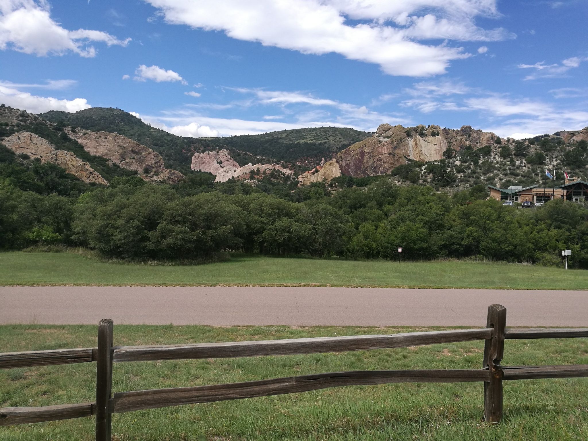 Wooden fence, green field, and road leading to rocky, tree-covered mountains. - Mesa Trail loop via Ivywild