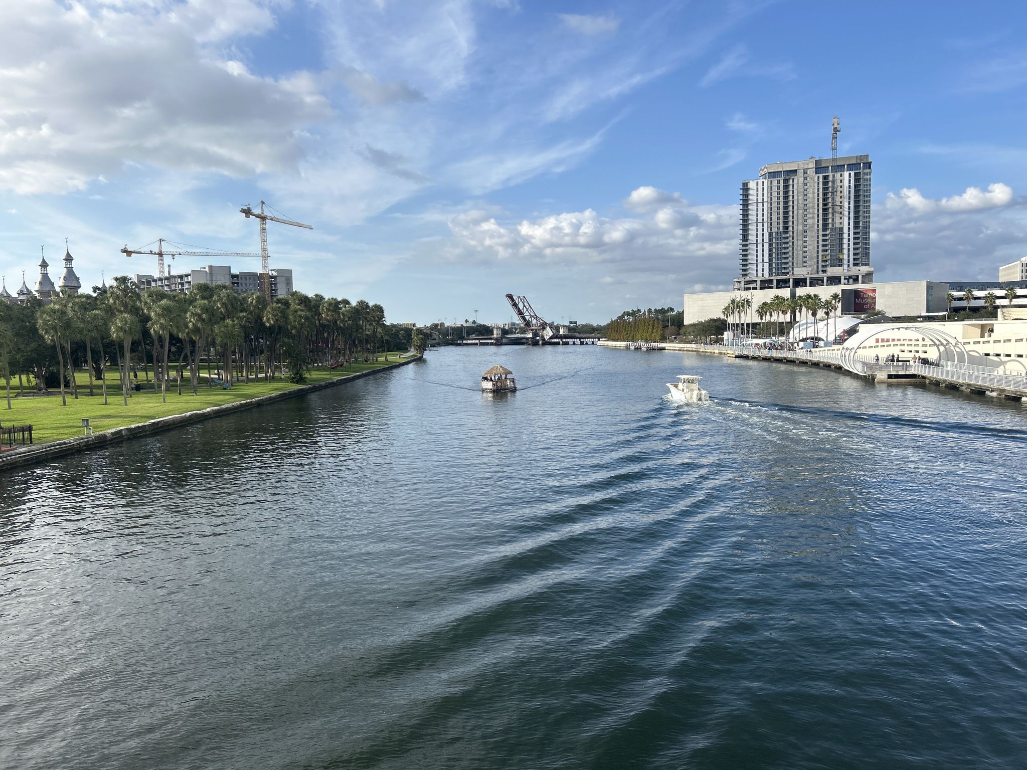 Boats navigate a wide river with an urban skyline under a bright, cloudy sky. - Tampa Riverwalk Trail