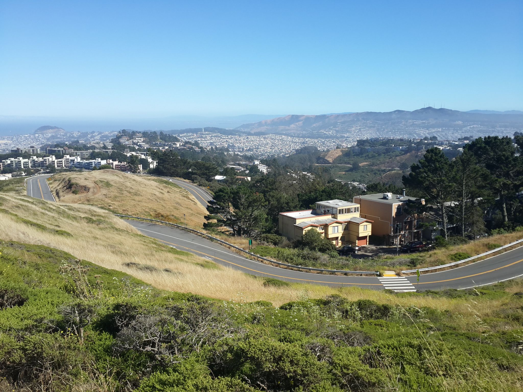 Winding road through grassy hills, with distant city and houses. - Twin Peaks - South/Noe Peak – Twin Peaks - North/Eureka Peak loop from Ocean Avenue & Jules Avenue