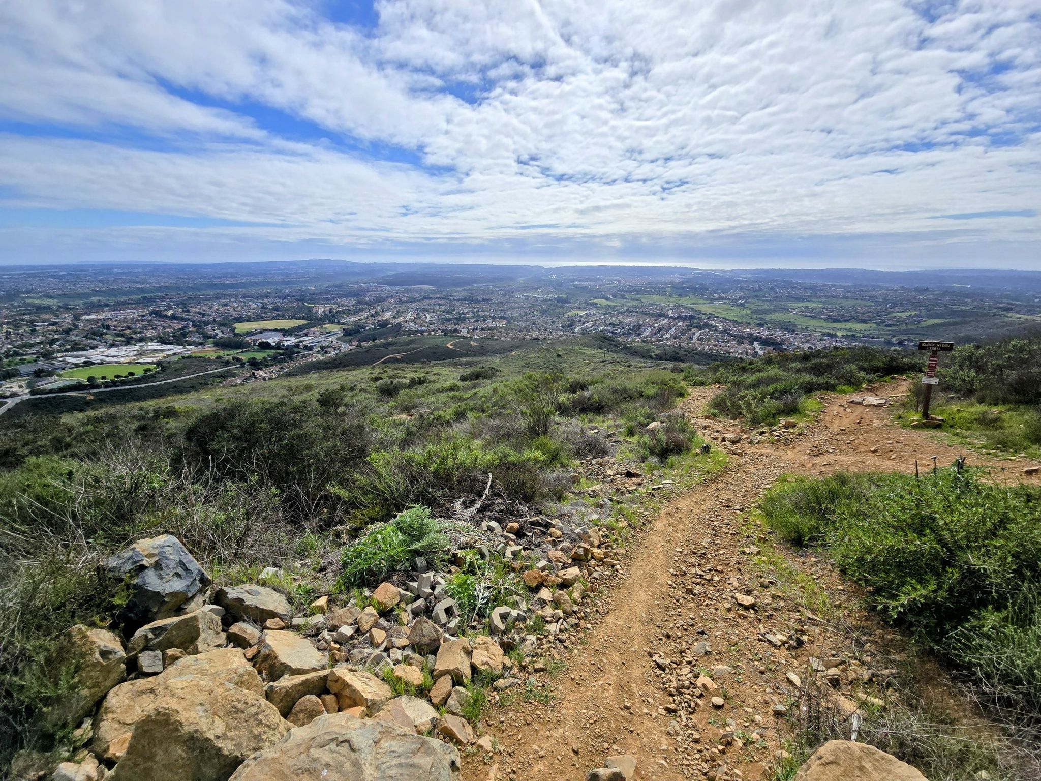 Dirt trail leads to a panoramic view of green hills and distant urban areas. - Black Mountain loop from Black Mountain Ranch