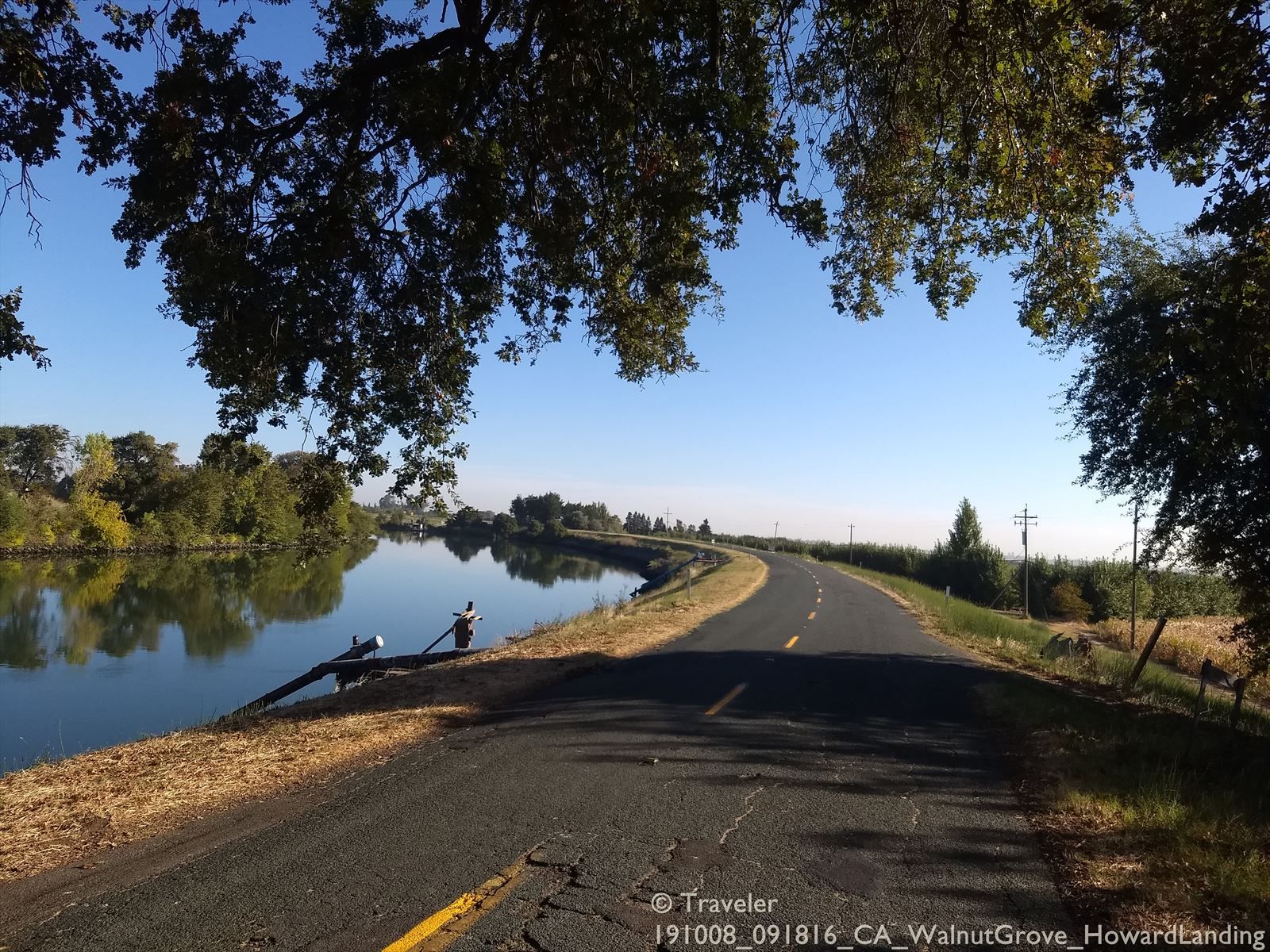 Paved road curves beside a calm river under a bright blue sky. - Sacramento River Double Loop