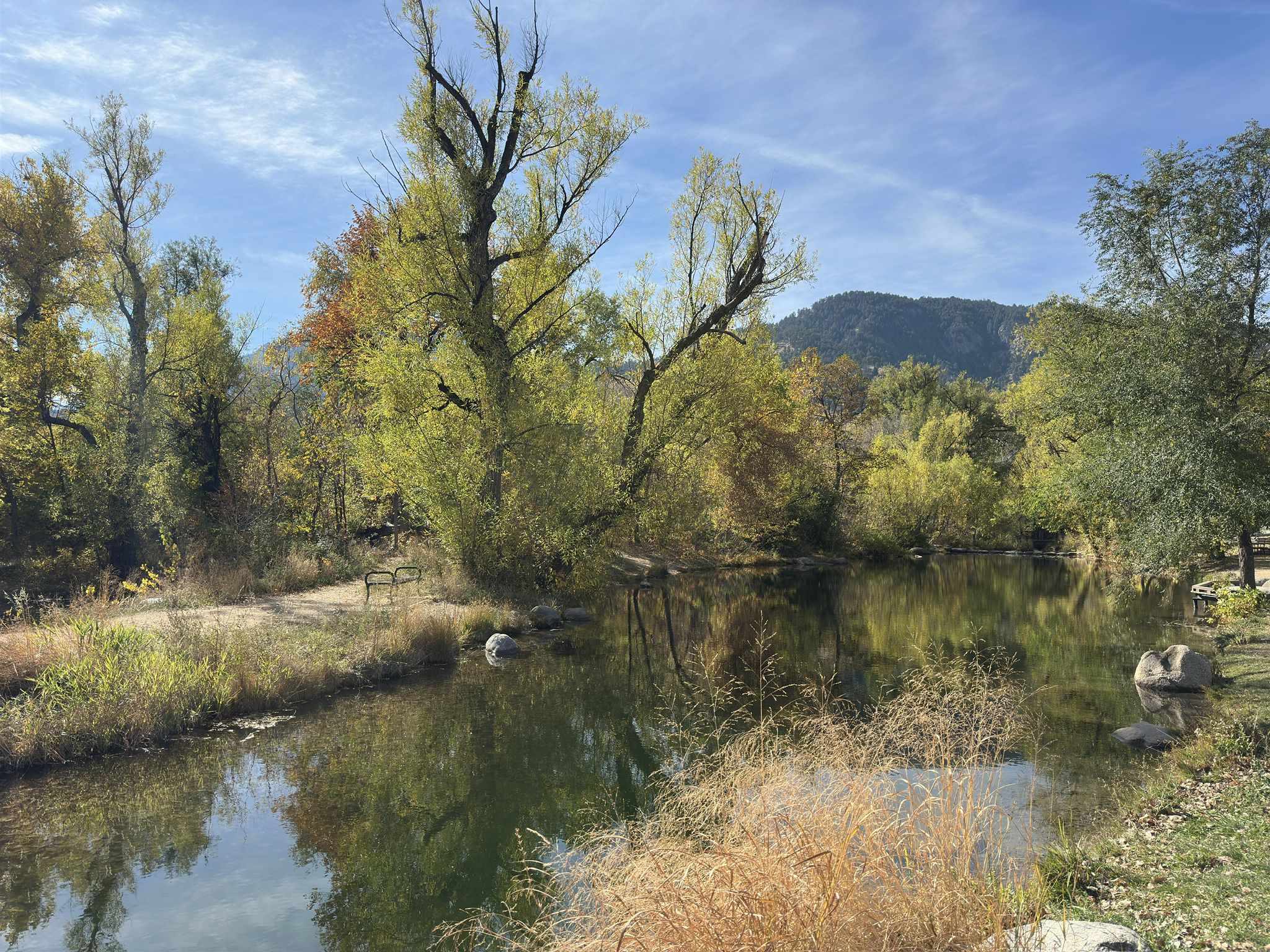 A calm pond reflects autumn trees and mountains on a sunny day. - Boulder Creek Path loop from Boulder