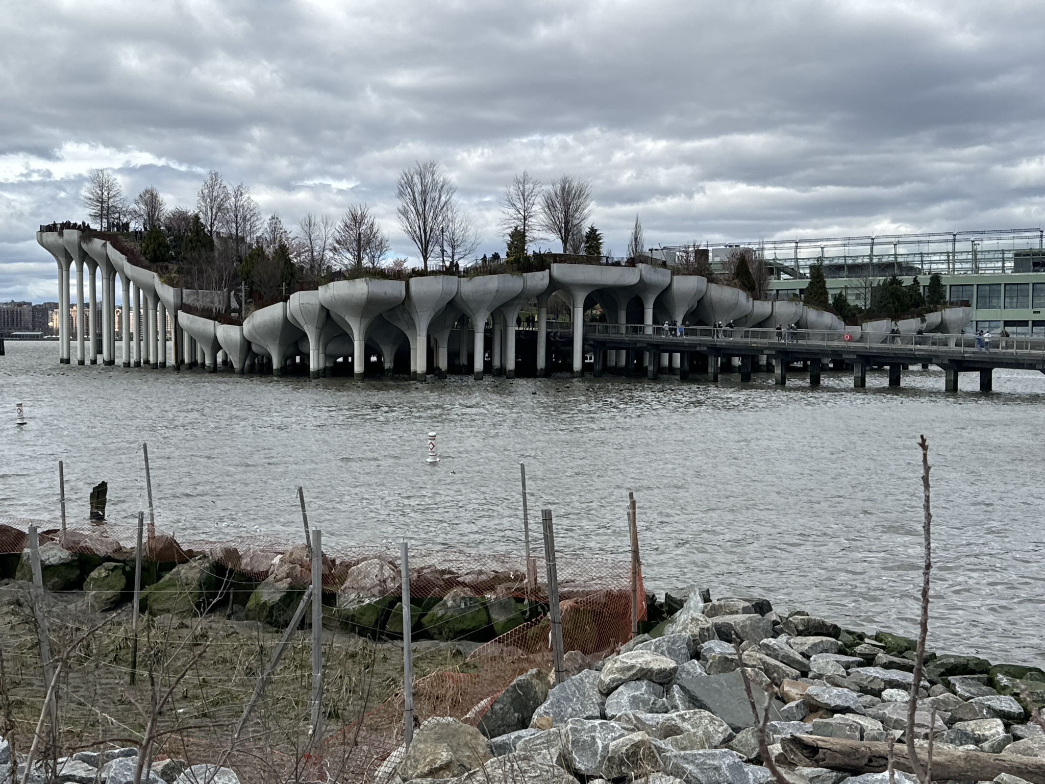 A unique, modern structure with trees over water, seen from a rocky shore. - Manhattan Waterfront Greenway