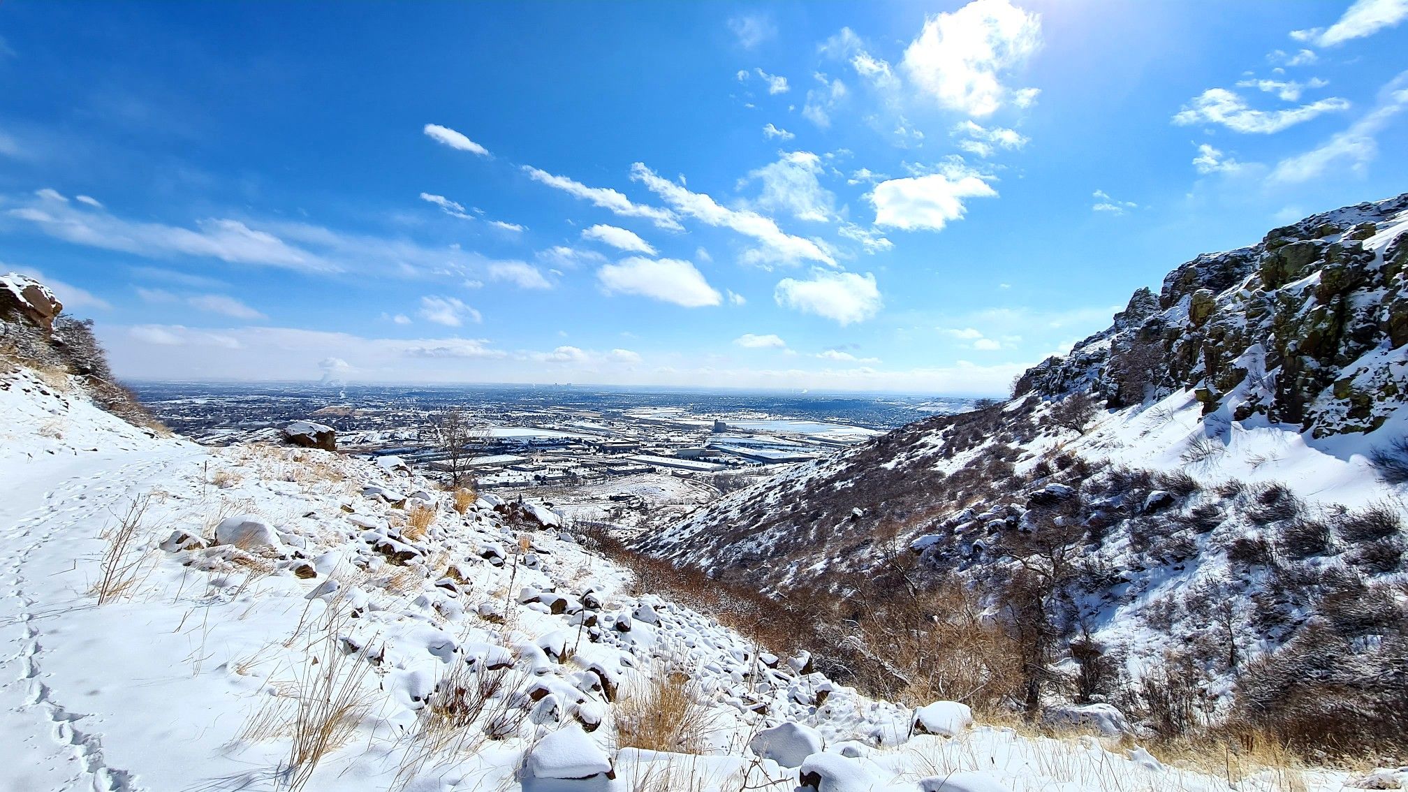 A snowy mountain valley with rocky slopes and a distant city view. - Lithic Trailhead – Downtown Denver View loop from Colorado Railroad Museum