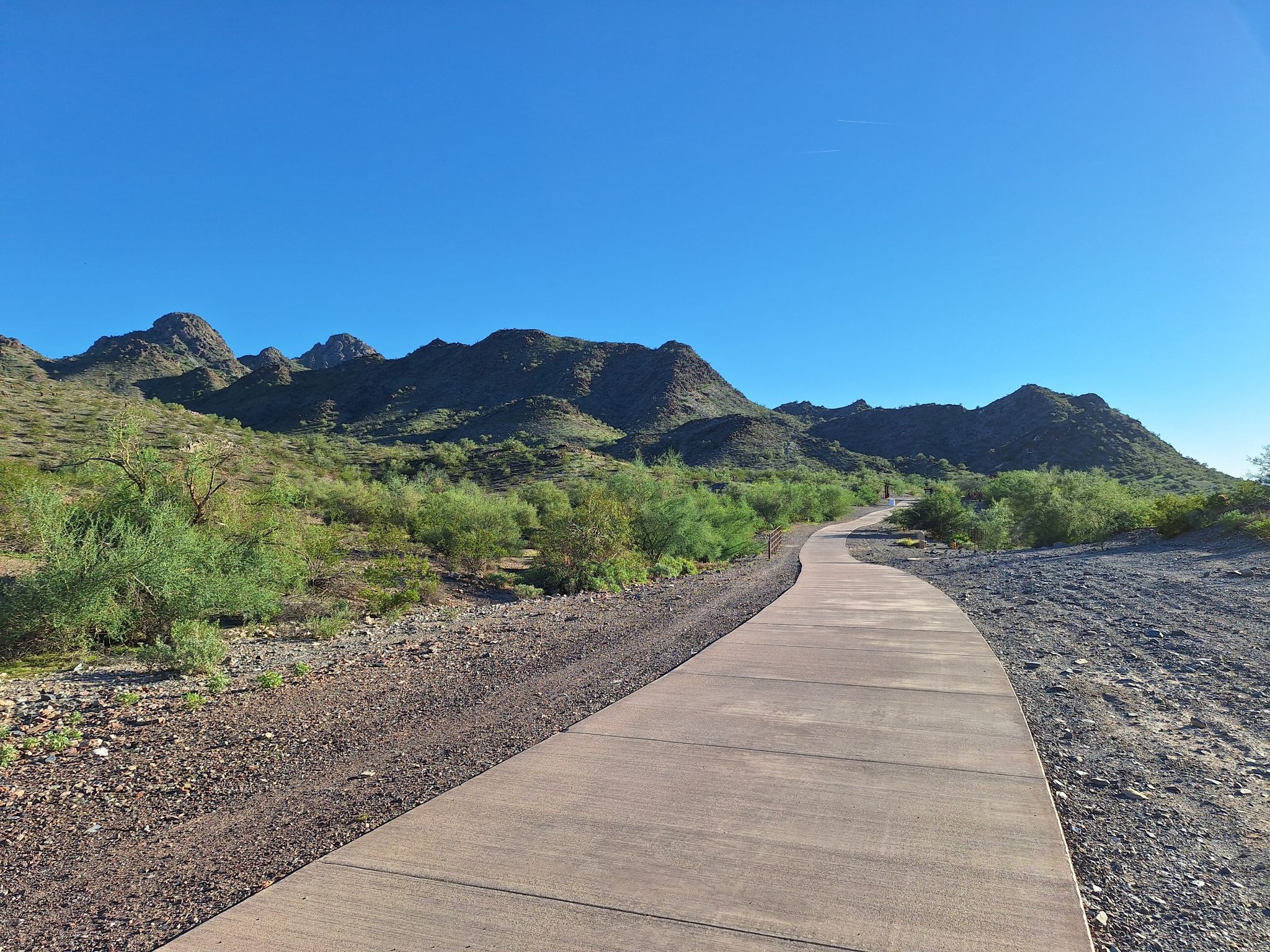 A wide paved path curves through green desert landscape towards distant mountains. - Phoenix Mountains Preserve – Phoenix Mountains Preserve loop from Walgreens