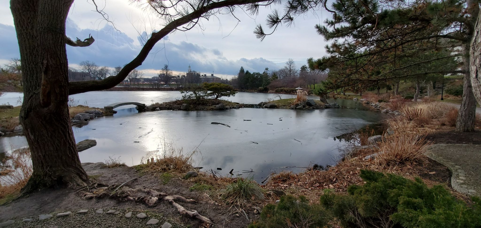 Partially frozen lake with small islands, a stone bridge, and bare trees. - Aqua Lane Park – Grand Island Bridges loop from Tonawanda