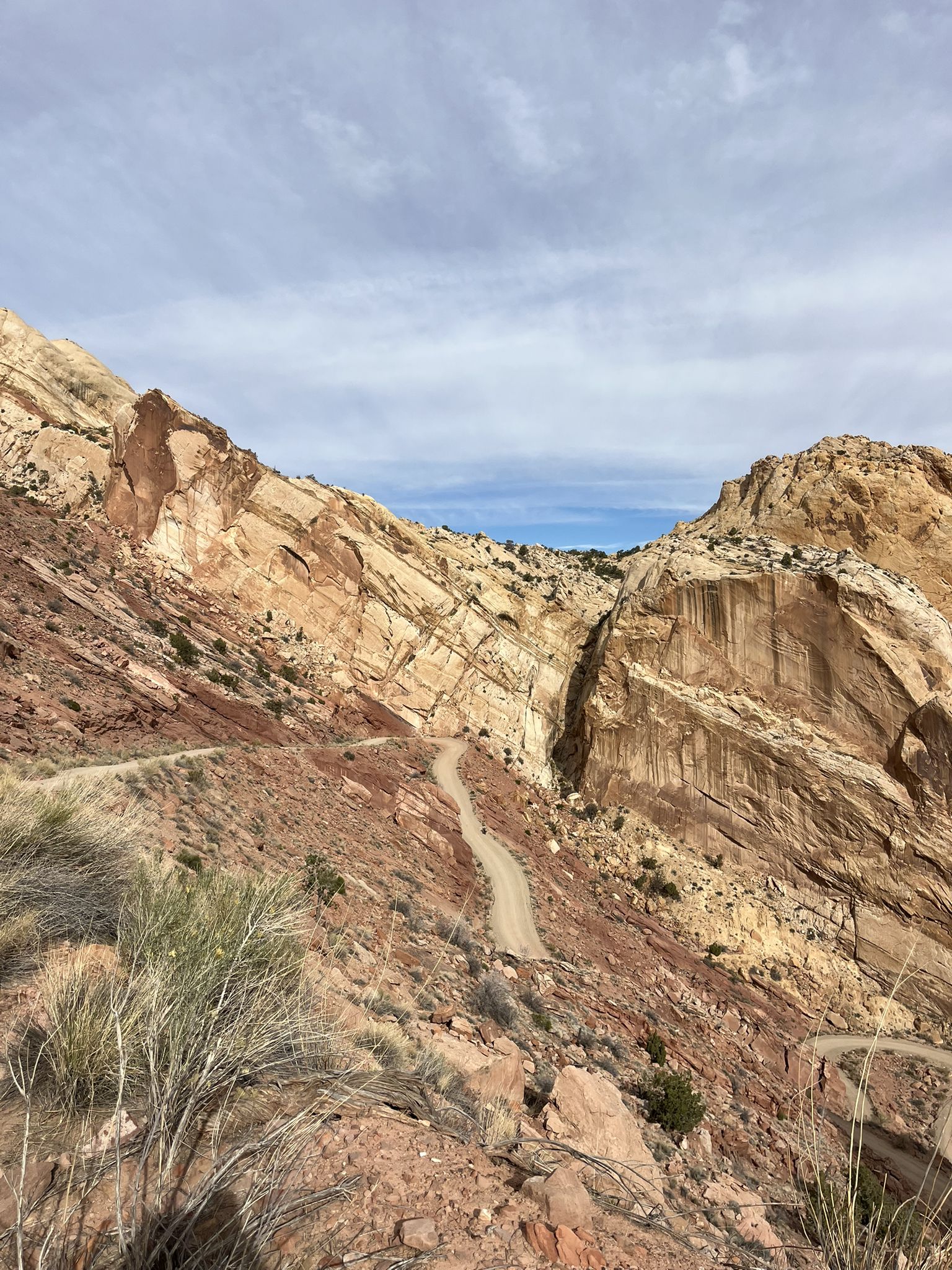 Dirt road winding through a steep, rocky canyon with towering stratified walls. - Burr Trail OHV Road