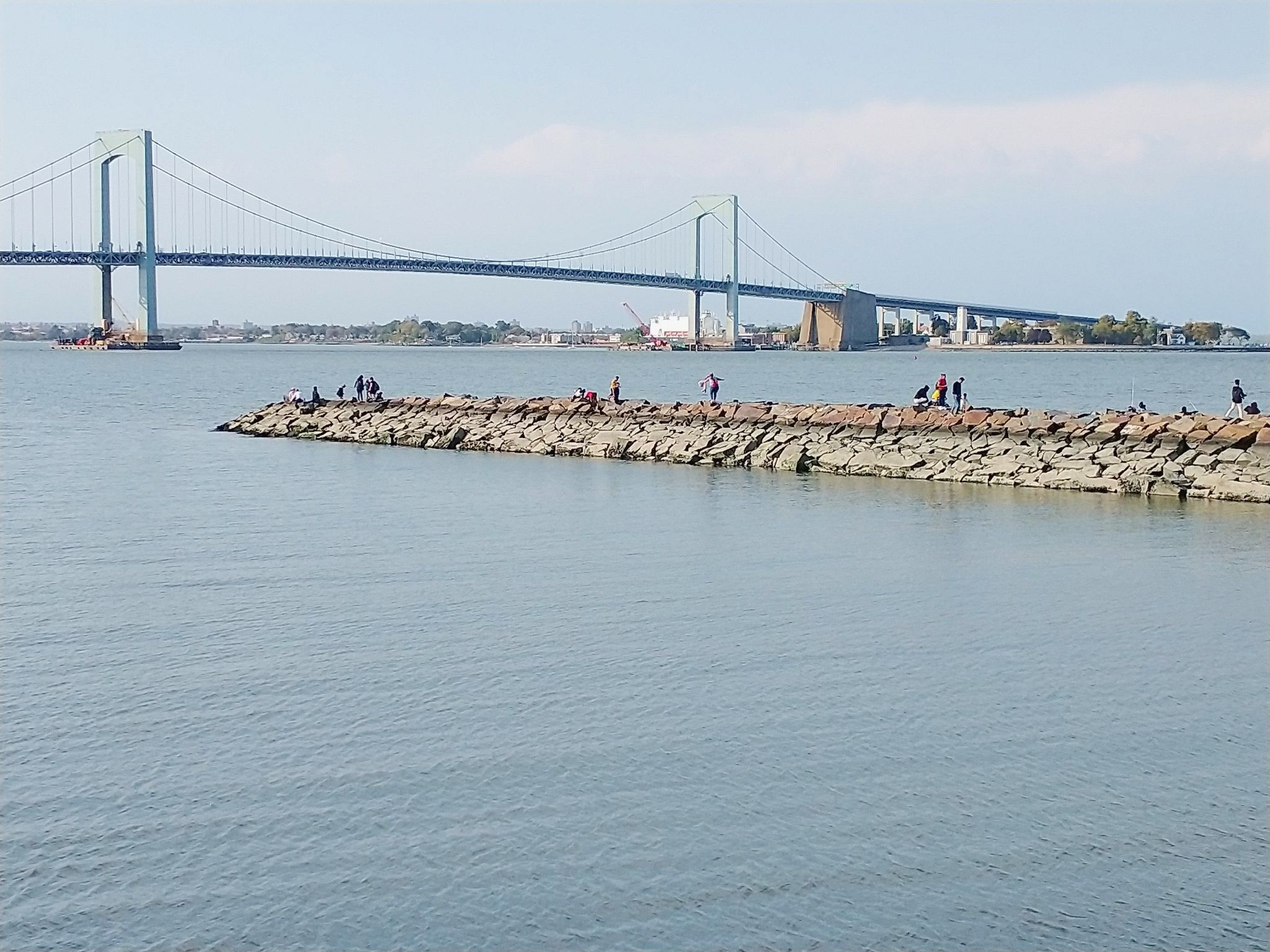 People fish on a rocky jetty with a large suspension bridge in the background. - Little Bay and Fort Totten Loop