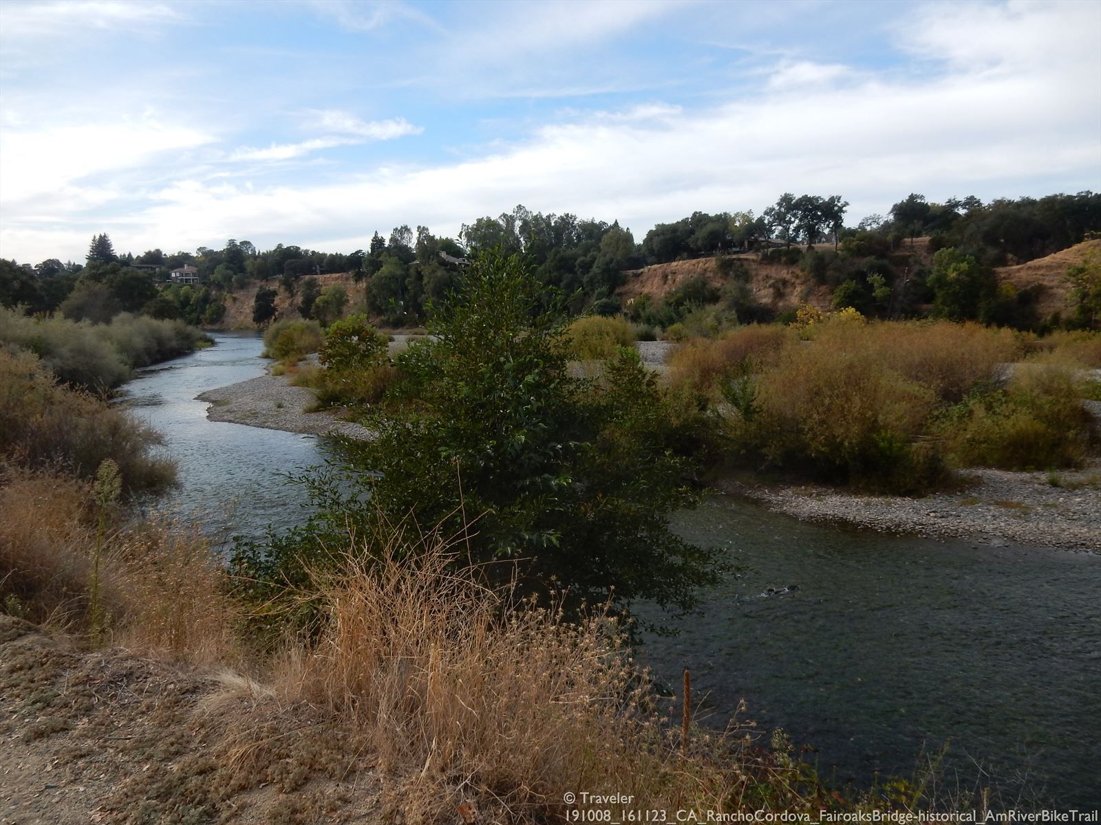 Winding river with rocky banks, dry grass, and green trees. - American River Bike Trail