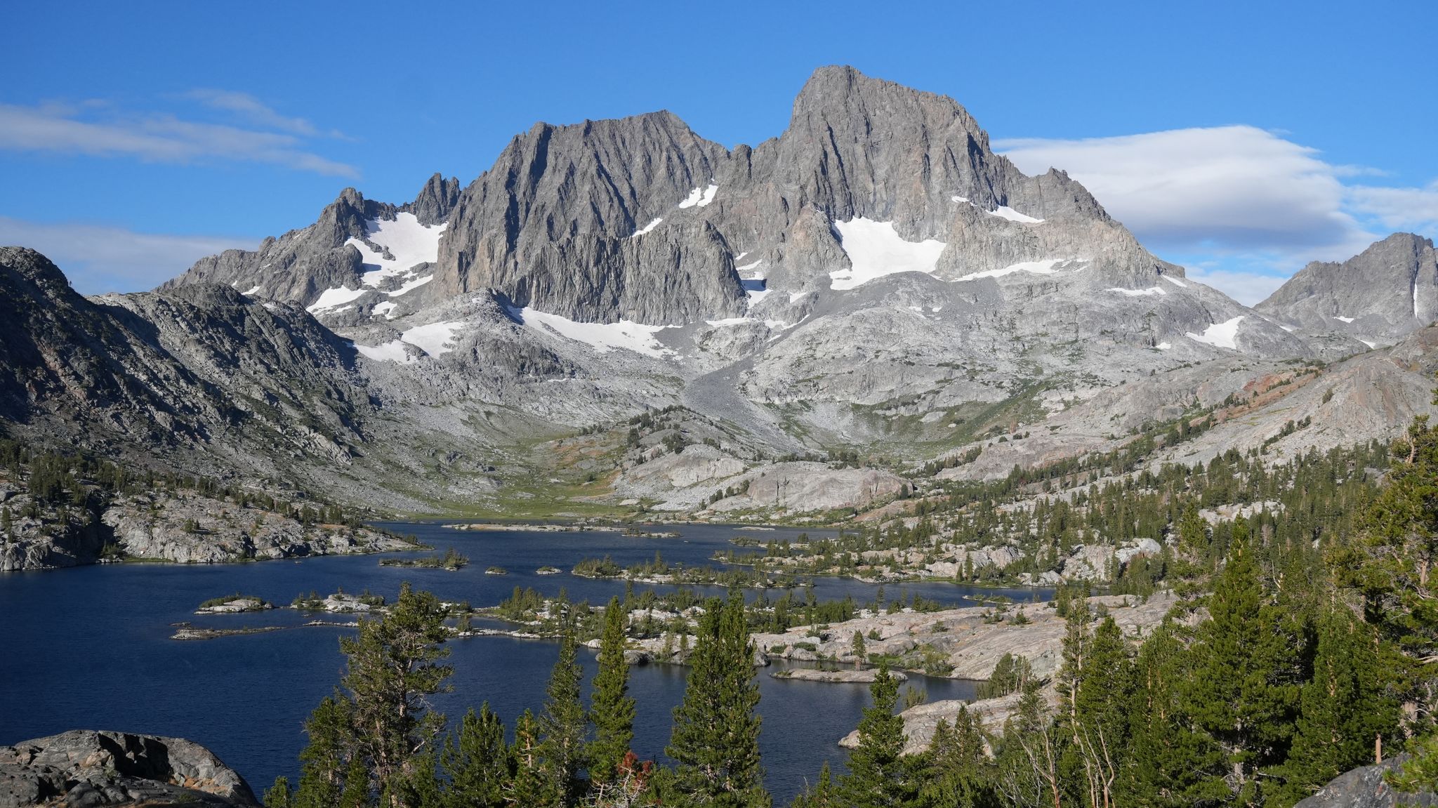 Majestic snow-dusted mountains rise above a serene lake surrounded by rocky terrain. - Shadow Creek Trail