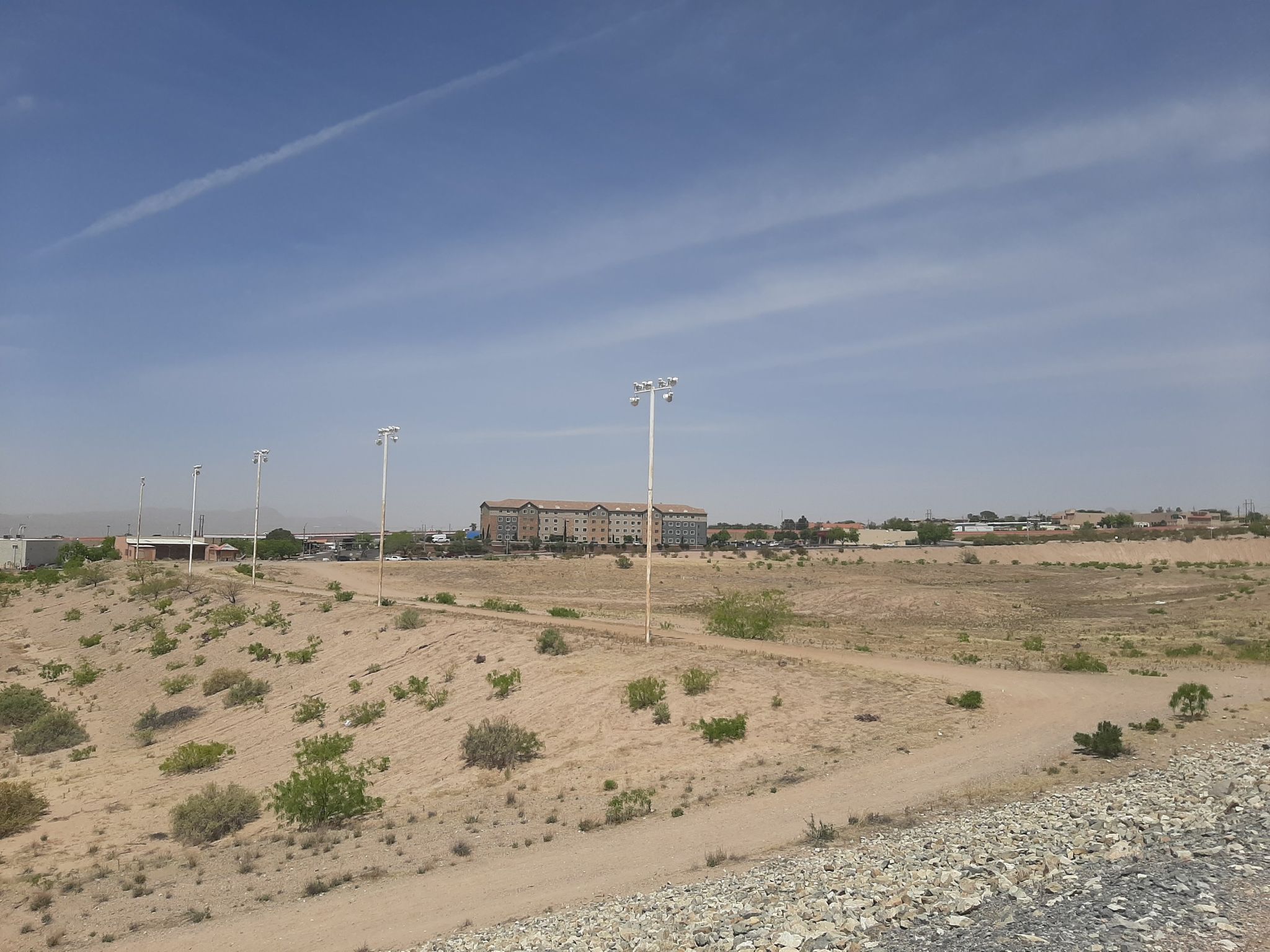 Desert landscape with distant buildings and light poles under a clear sky. - Las Cruces Dam – Dam Trail loop from Shell
