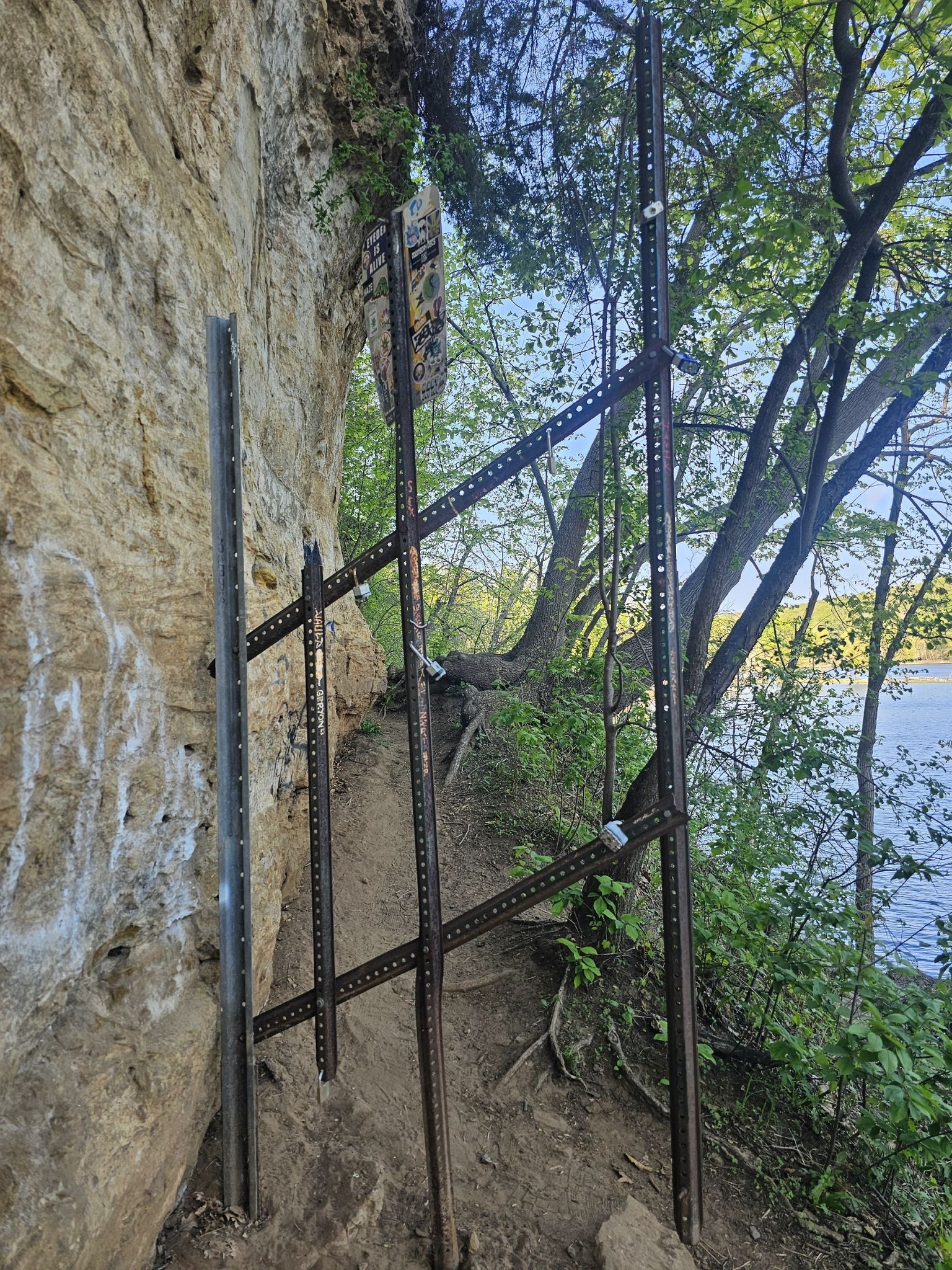 Metal posts secured to a rocky cliffside path overlooking water and trees. - St. Croix Boom Site Waterfall Trail