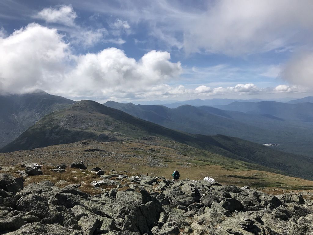 A hiker traverses a rocky mountain ridge under a partly cloudy sky. - Mount Jefferson Loop via Caps Ridge Trail