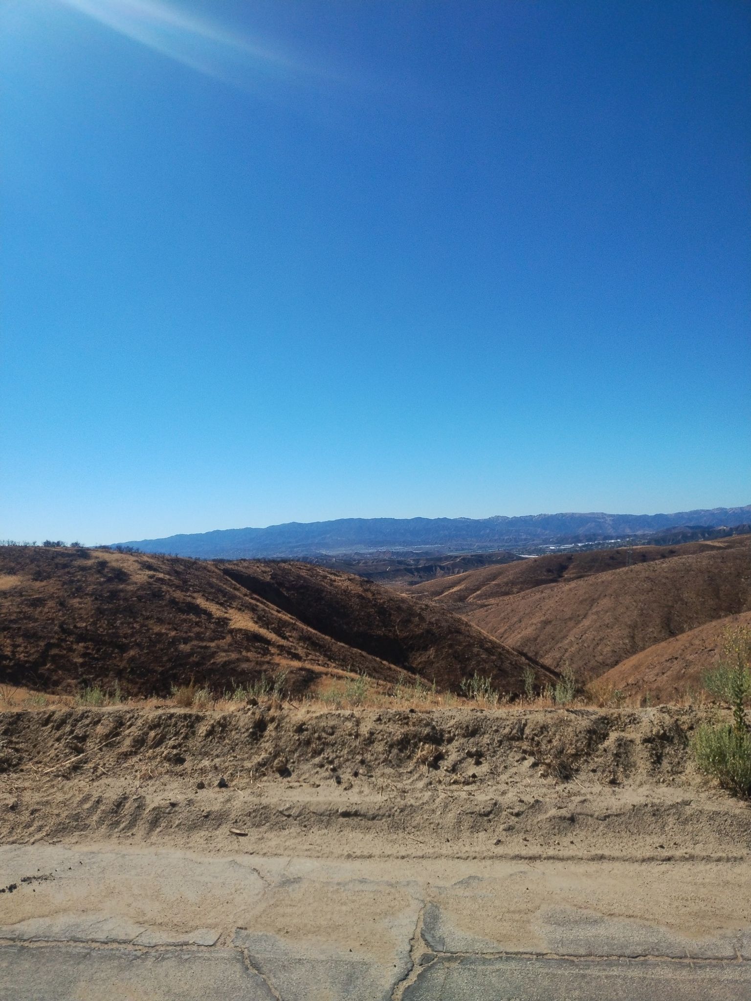Expansive view of dry, rolling hills under a bright blue sky with sun flare. - Lake Elizabeth – San Francisquito Canyon Road loop from Castaic
