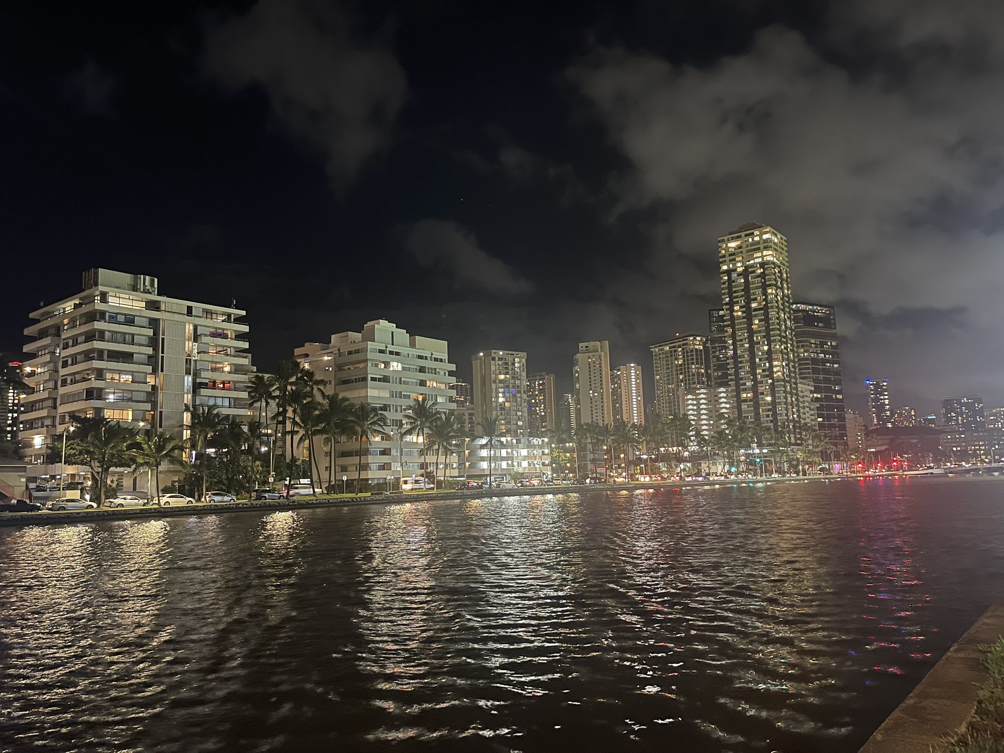 City skyline illuminated at night, reflecting on dark, calm water. - Ala Wai Park Trail – Tantalus Drive loop from Hanauma Bay