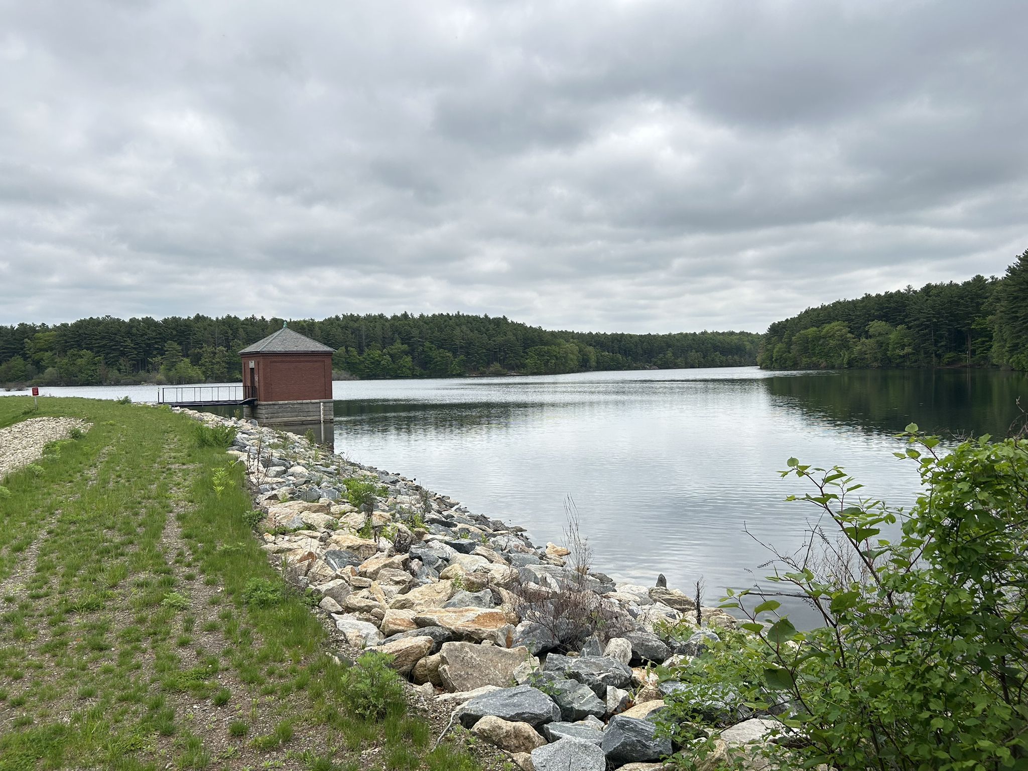 Overcast view of a calm lake with a small building and forested banks. - Mountain Bike Loop