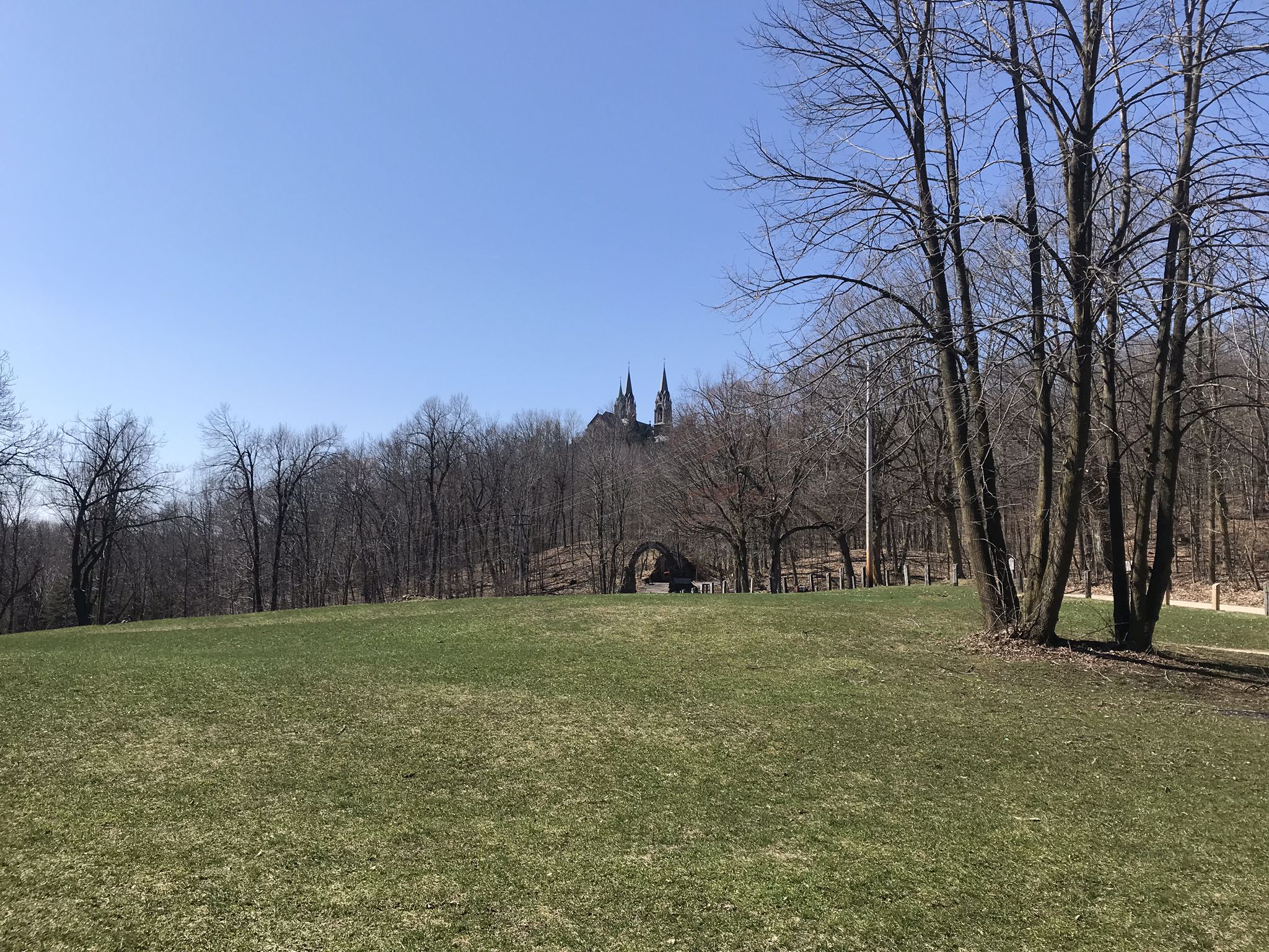 Grassy field with bare trees, a distant building visible under a clear sky. - Holy Hill loop from Holy Hill National Shrine of Mary, Help of Christians