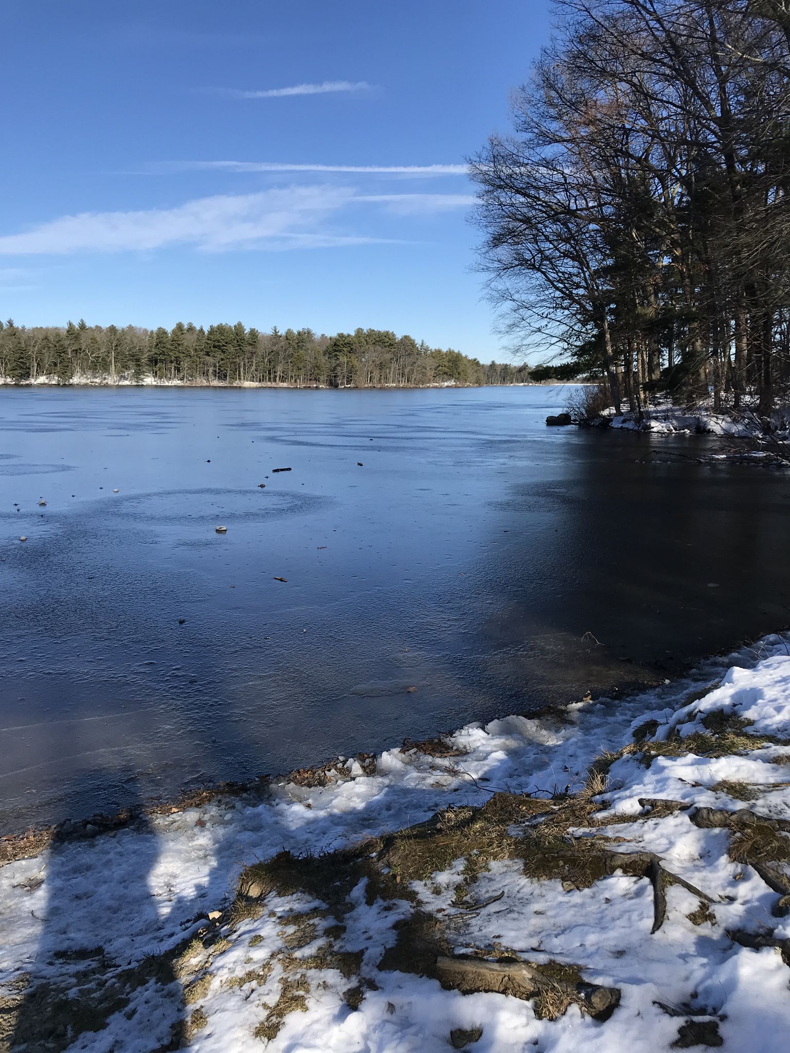 A partially frozen lake with snow on the shore under a bright blue sky. - Ashland Reservoir Trail