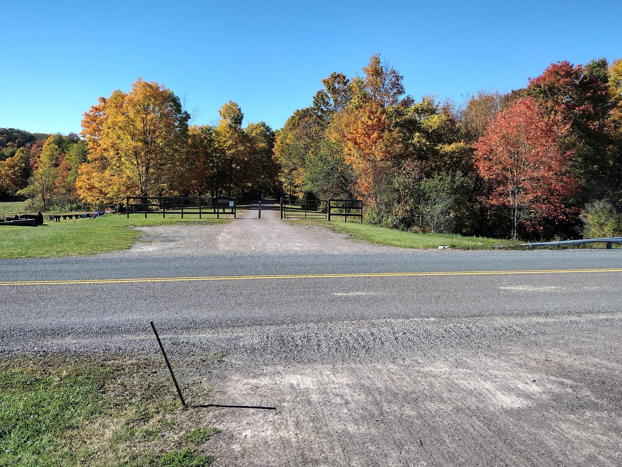 Paved road in front of a gated dirt entrance surrounded by autumn trees. - Meyersdale Visitors Center – Big Savage Tunnel loop from Meyersdale