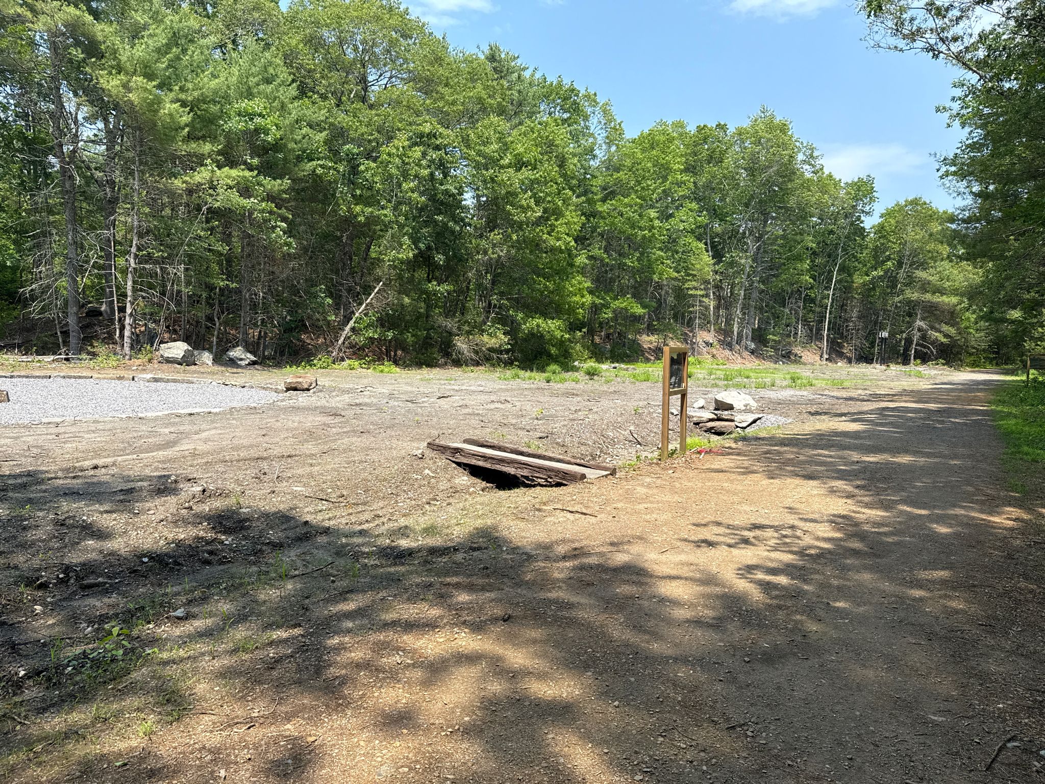 A dirt clearing with a small wooden culvert and distant green forest. - Air Line State Park Trail