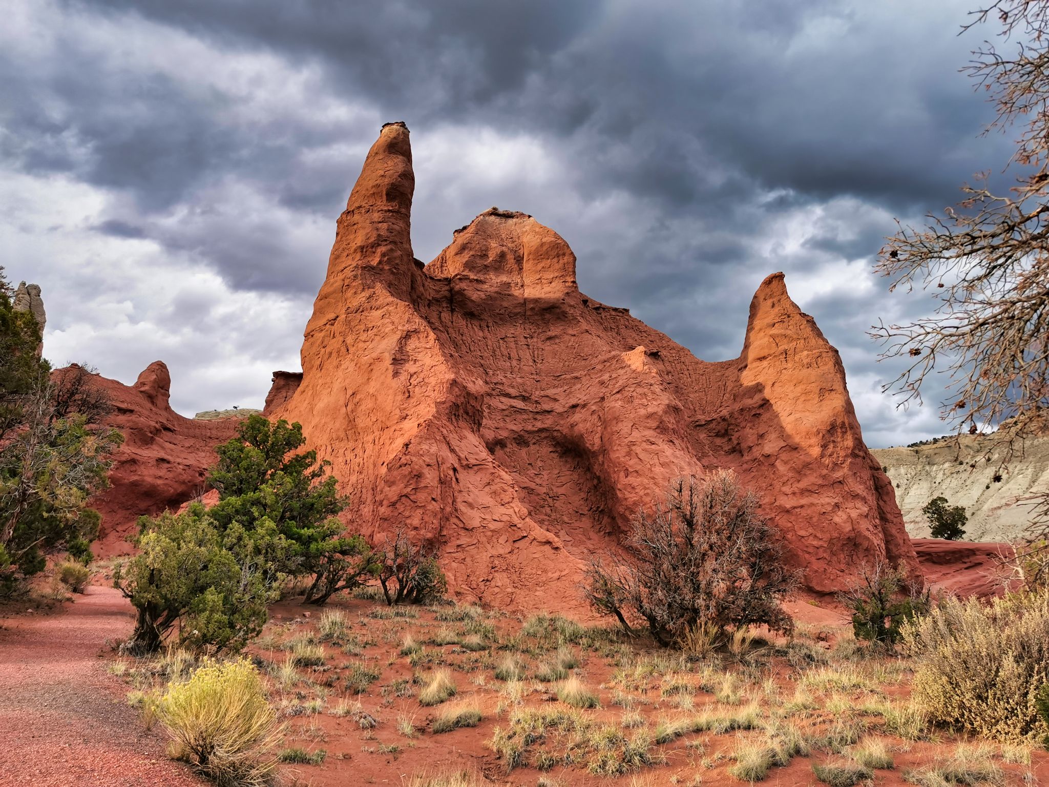 Large red rock formation with a pointed peak under a dramatic cloudy sky. - Kodachrome Nature Trail – Ballerina Spire loop from Kodachrome Basin State Park