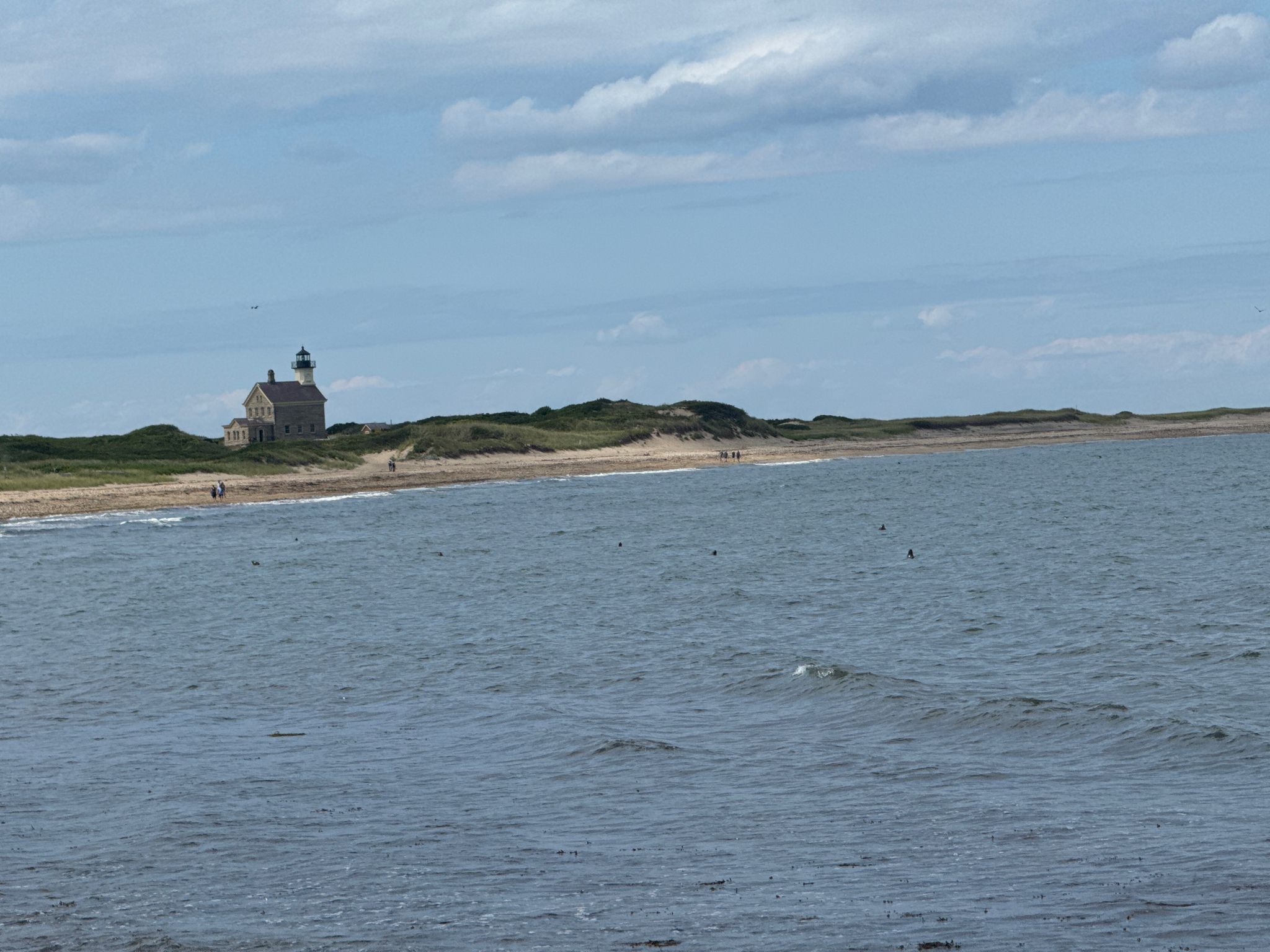 Distant lighthouse on a sandy shore with ocean in foreground under cloudy sky. - North Lighthouse Trail