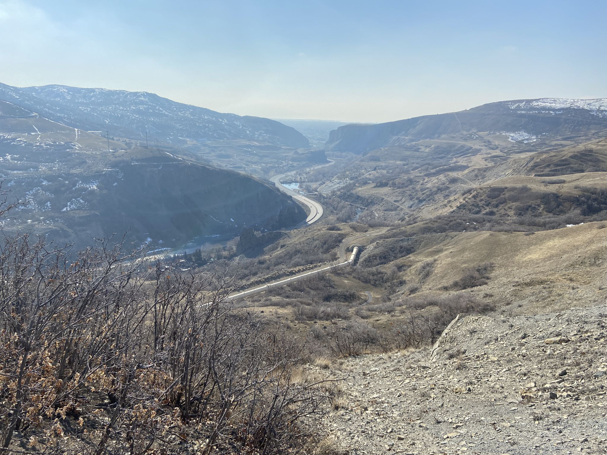 Wide valley view with a winding road, river, and distant hazy mountains. - Provo River Parkway – Bridal Veil Falls loop from Orem