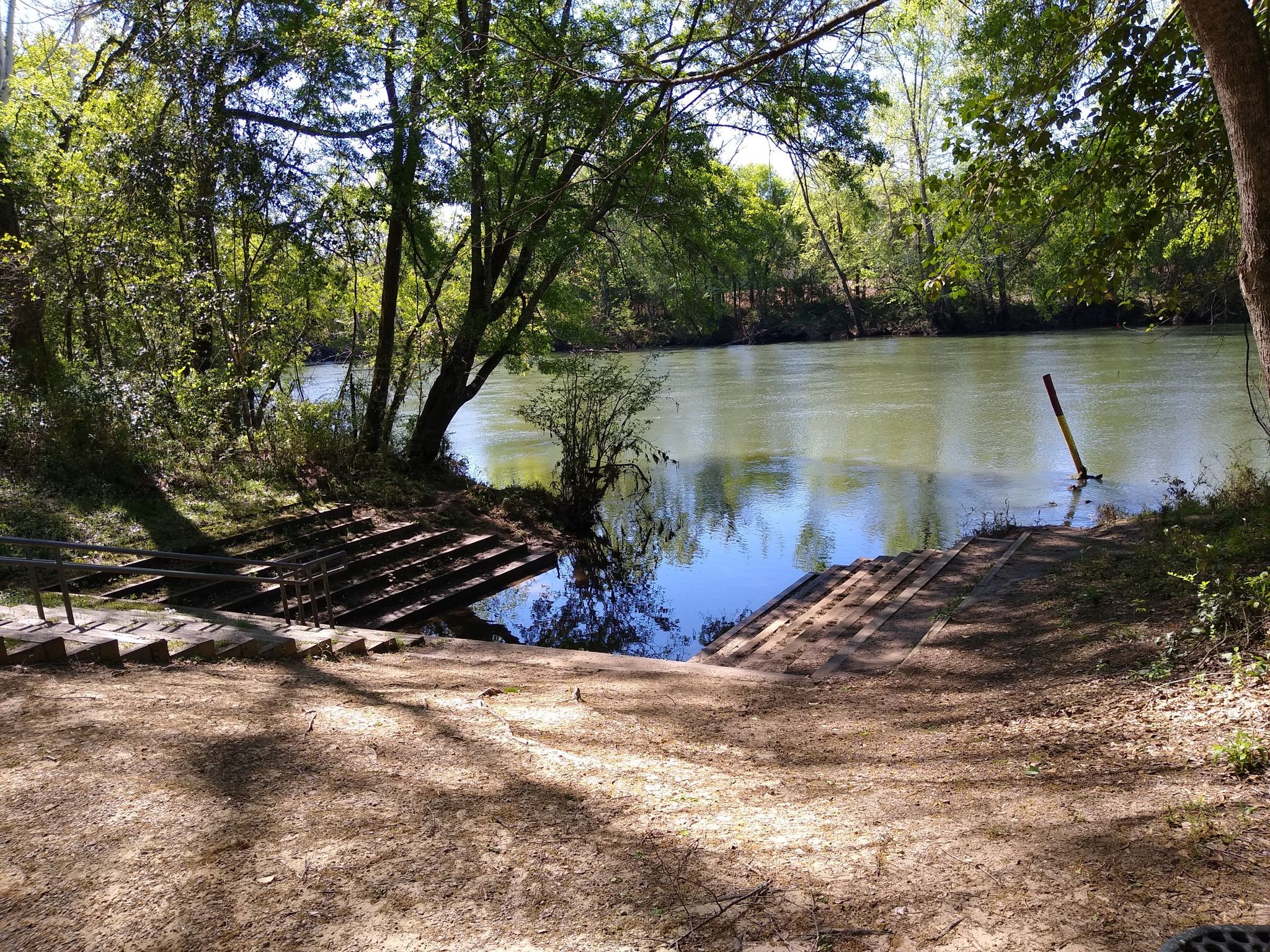 Dirt and wooden boat ramp leading into a wide, calm river. - Greenway Trail
