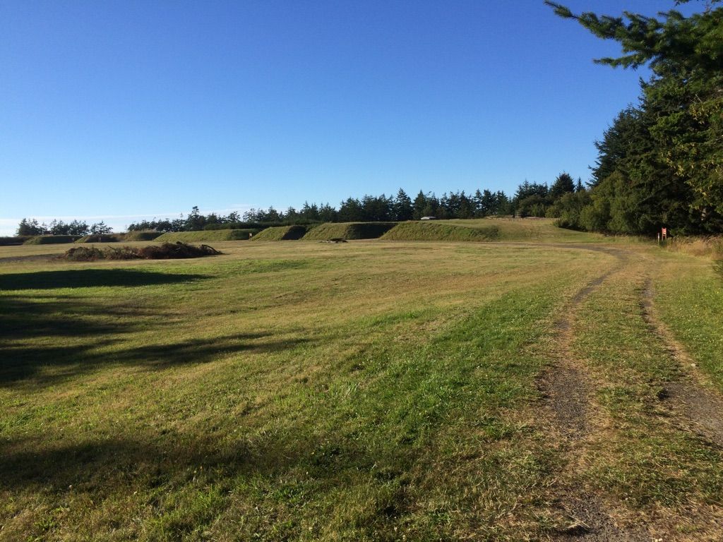 Grassy field with rolling mounds and a dirt path under a clear sky. - Fort Flagler Trail loop Run