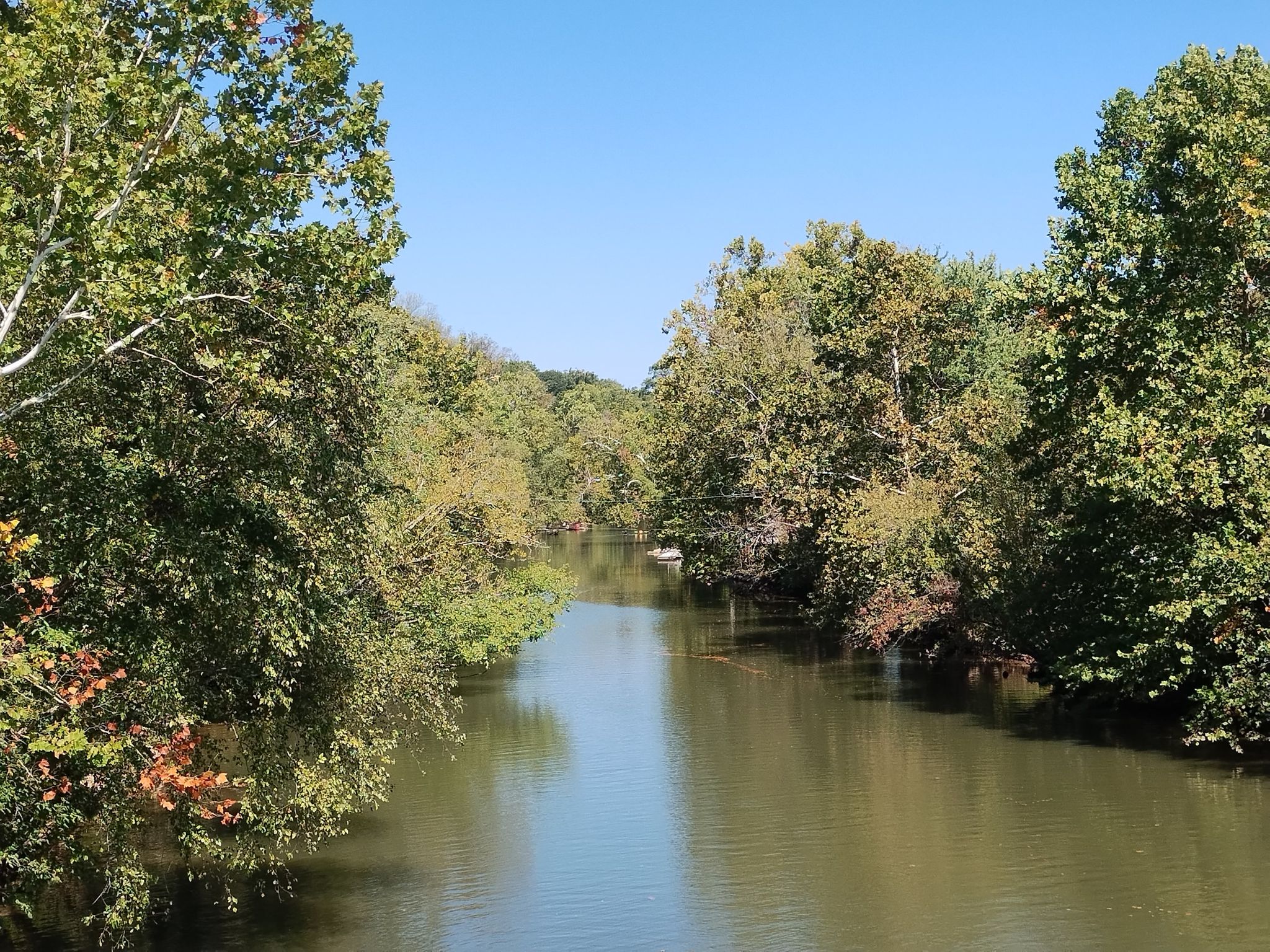 Calm river flowing between lush green trees under a clear blue sky. - Riley’s lock – John Poole House loop from Seneca
