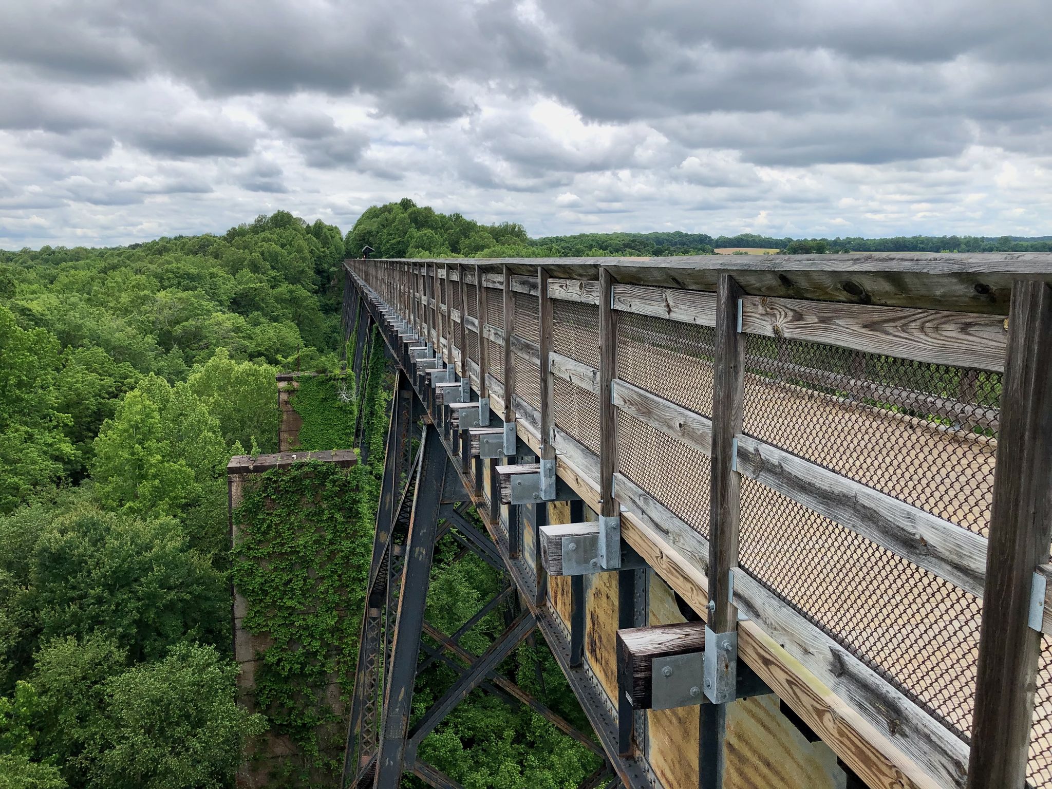 A long, tall bridge extends over a lush green forest under cloudy skies. - High Bridge Trail – High Bridge loop from Camp Paradise