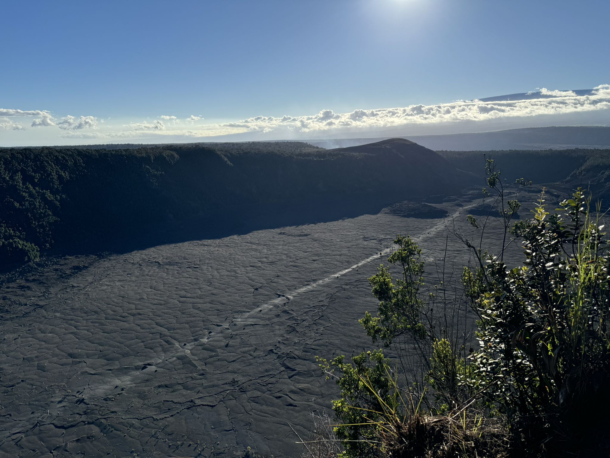 A vast, dark volcanic crater floor under a bright, sunny sky. - Crater Rim to Kīlauea Iki Overlook
