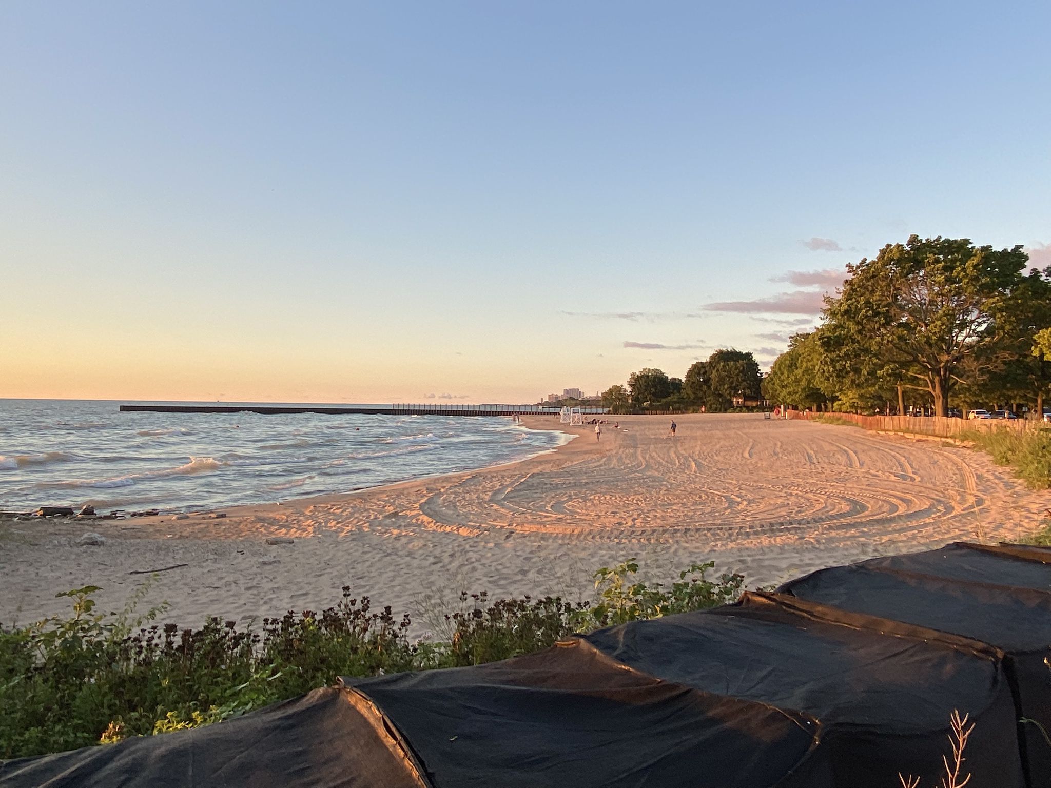 Sandy beach and calm water at sunset with a distant pier and people. - Burnham Shores Park – Lee Street Beach loop from Davis