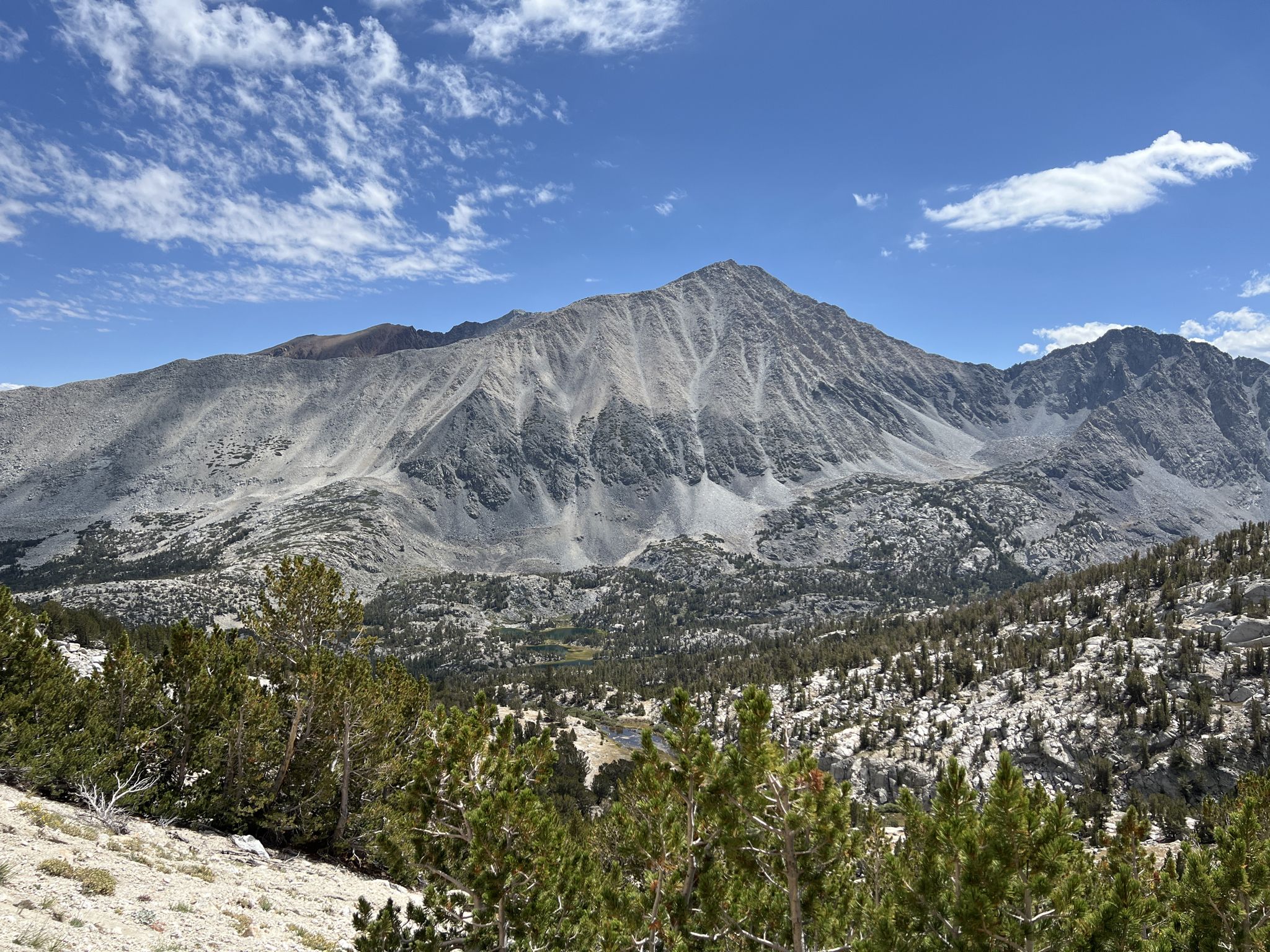 Majestic rocky mountain overlooks a forested valley under a bright sky. - Mono Pass Trail