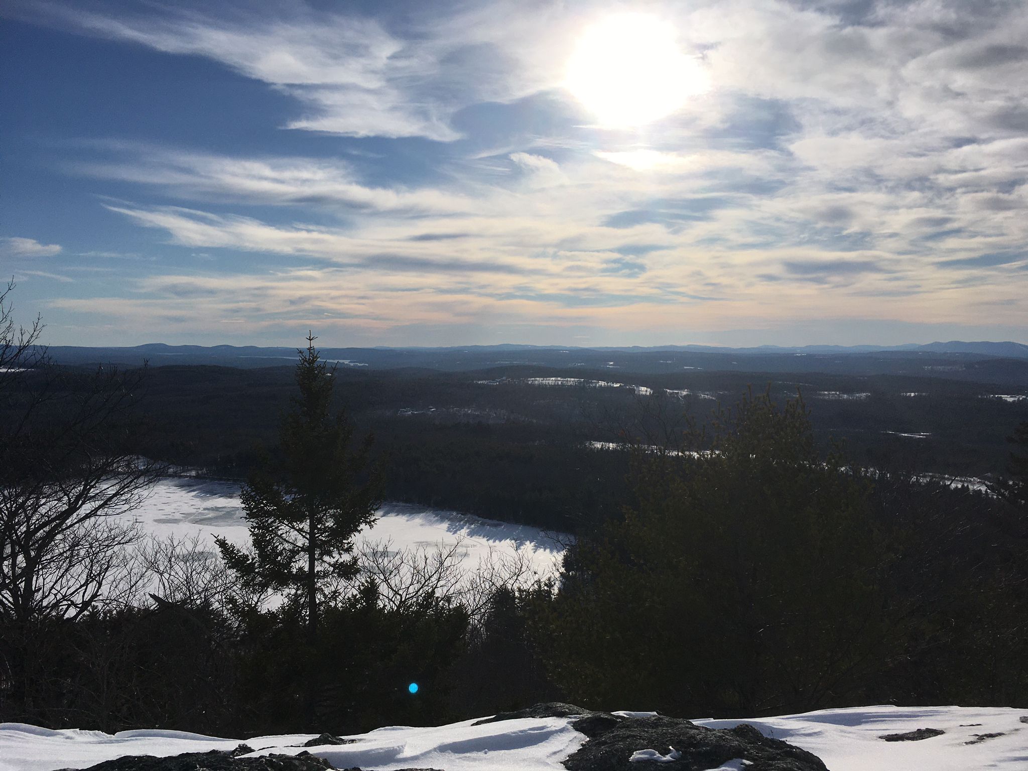 Panoramic winter view from a snowy peak, bright sun over a frozen lake and distant hills. - Hall Pond and Singepole Mountain Trail