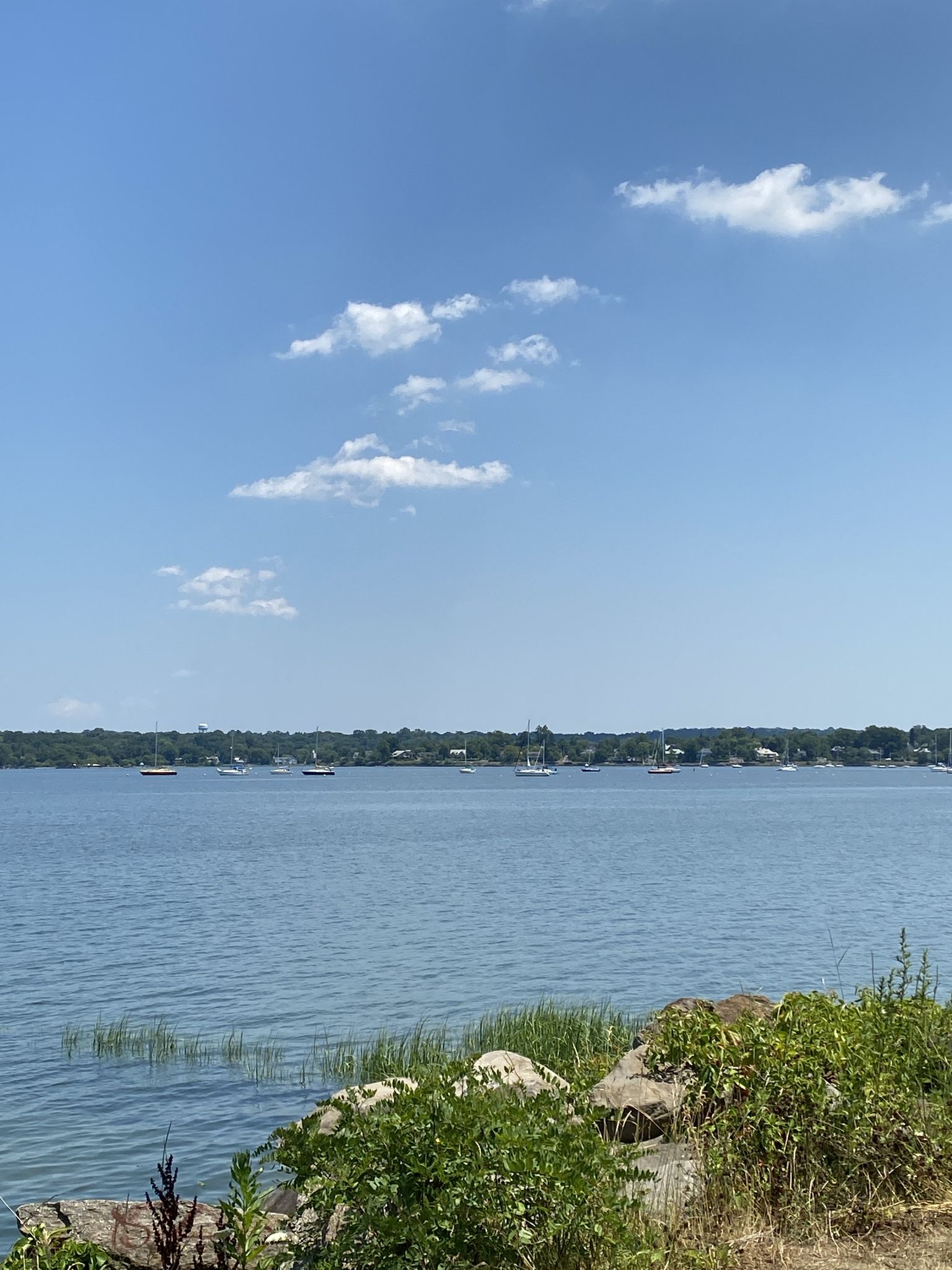 Calm water with distant boats, rocky foreground, and blue sky. - Fort Totten Lake – Little Bay Park loop from Throgs Neck Bridge