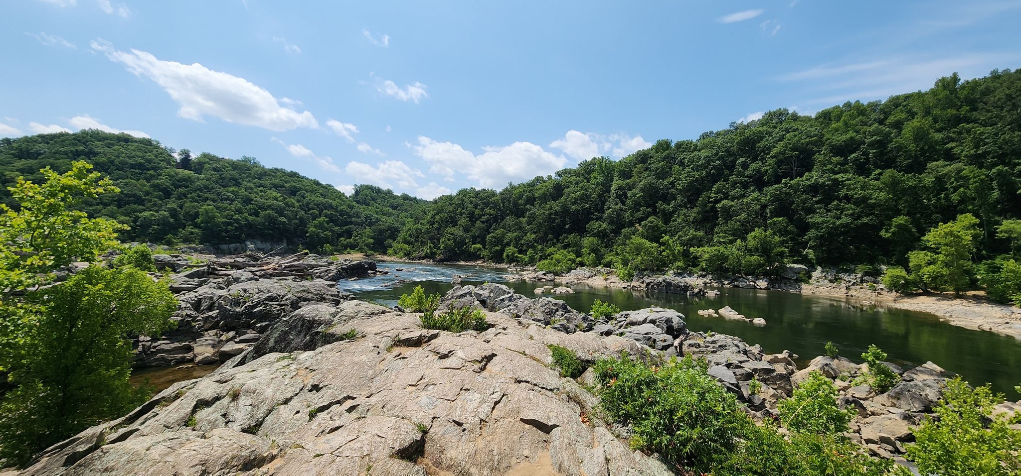 River flowing through rocky terrain, surrounded by lush green hills under a blue sky. - Great Falls Overlook via Billy Goat Trail Section A