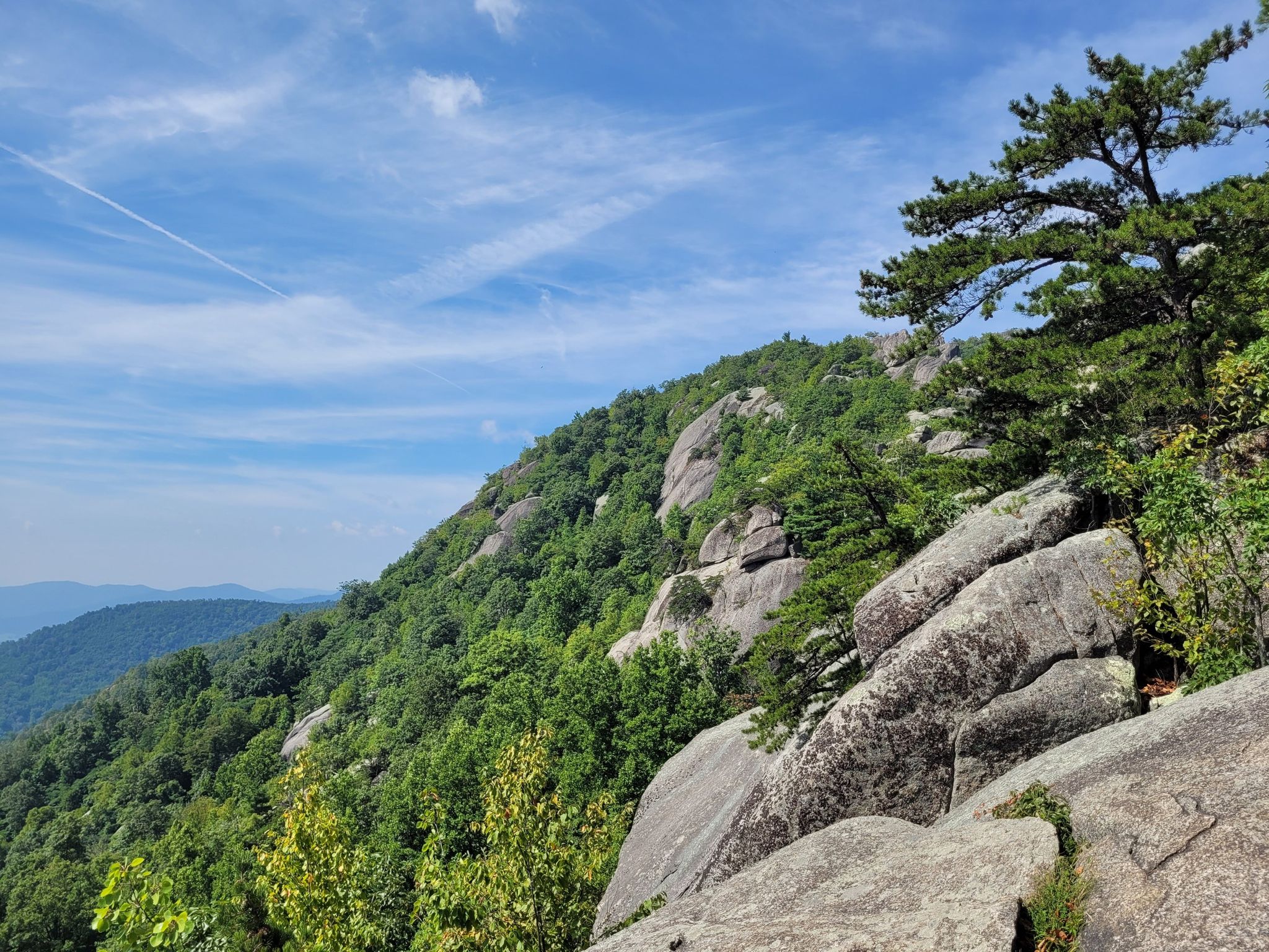 Mountain slope with large boulders, green trees, and blue sky with wispy clouds. - Old Rag and Robertson Mountain Loop