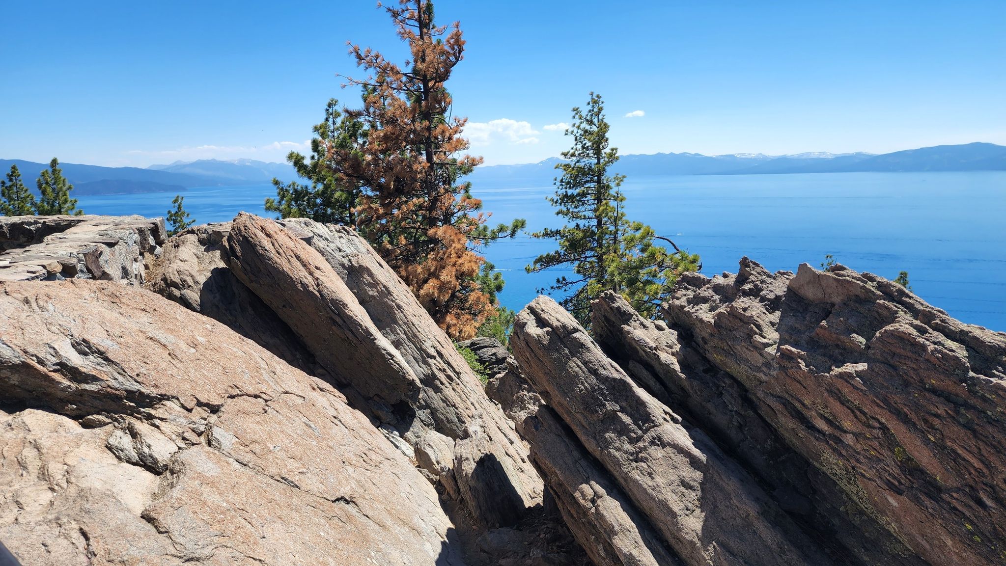 Jagged rocks overlook a vast blue lake and distant mountains. - Stateline Lookout