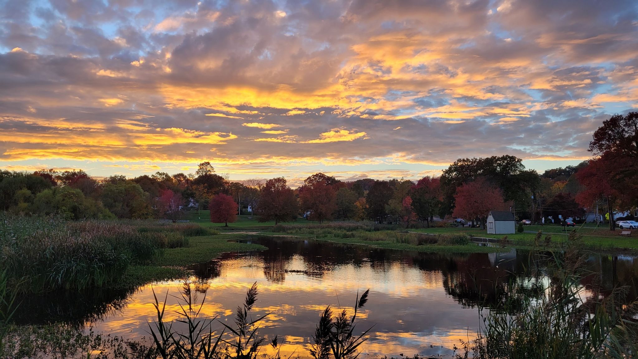 Vibrant sunset over a calm pond reflecting colorful autumn trees and sky. - Briant Park Loop